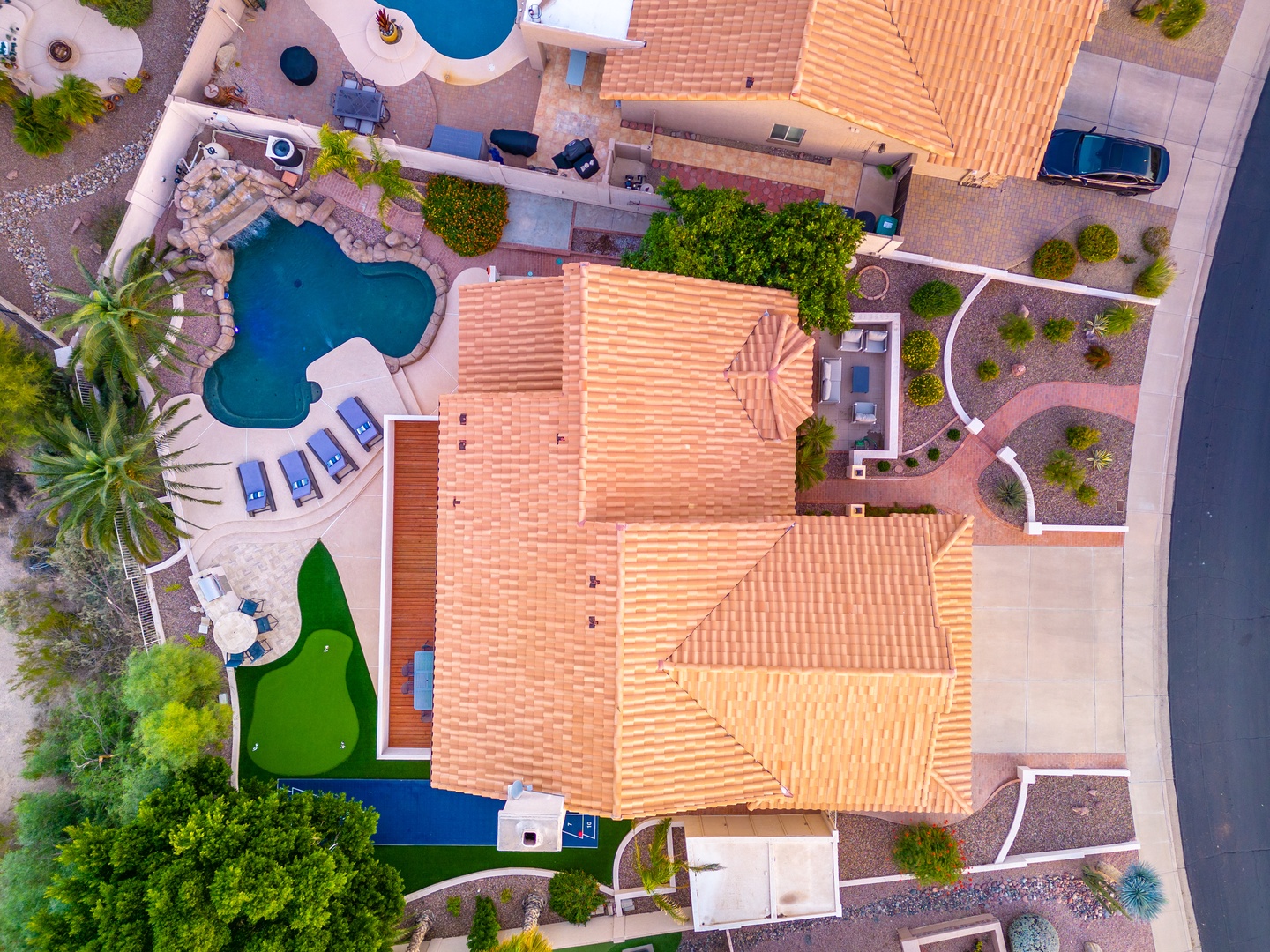 Aerial view showcasing the property's striking Spanish tile roofing, multiple pools, putting green, and meticulously landscaped grounds in a peaceful desert setting.