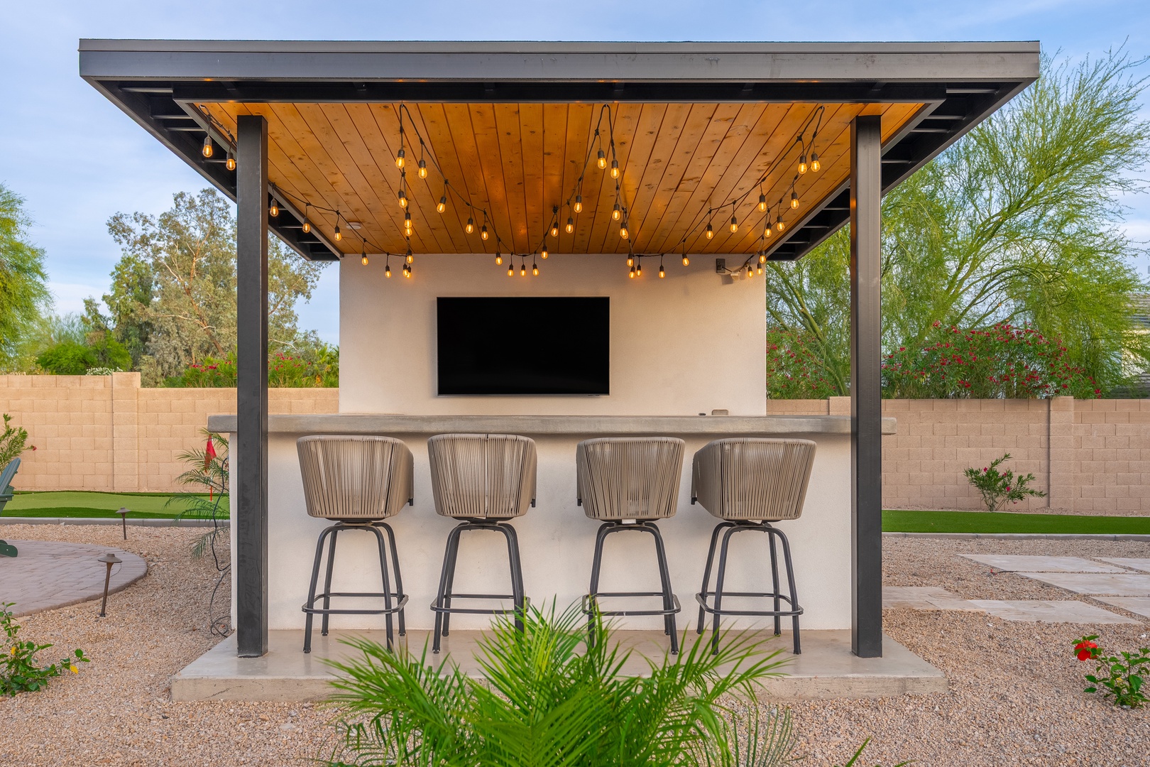 Your own backyard bar awaits under warm string lights, with sleek seating and a big screen for unforgettable evenings under the stars.