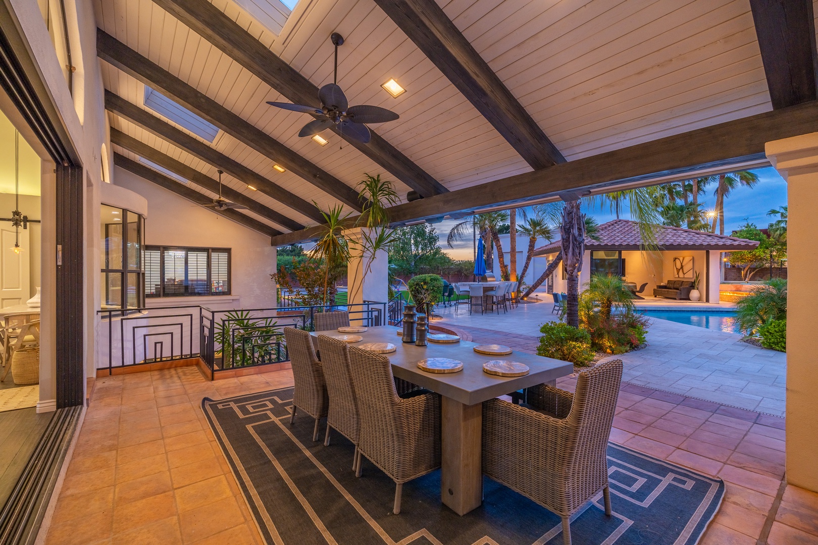Picture yourself dining al fresco under soaring wood-beamed ceilings while the evening light filters through palms. Your private covered patio seamlessly connects to a sparkling pool, lush tropical landscaping, and additional entertaining spaces—perfect f