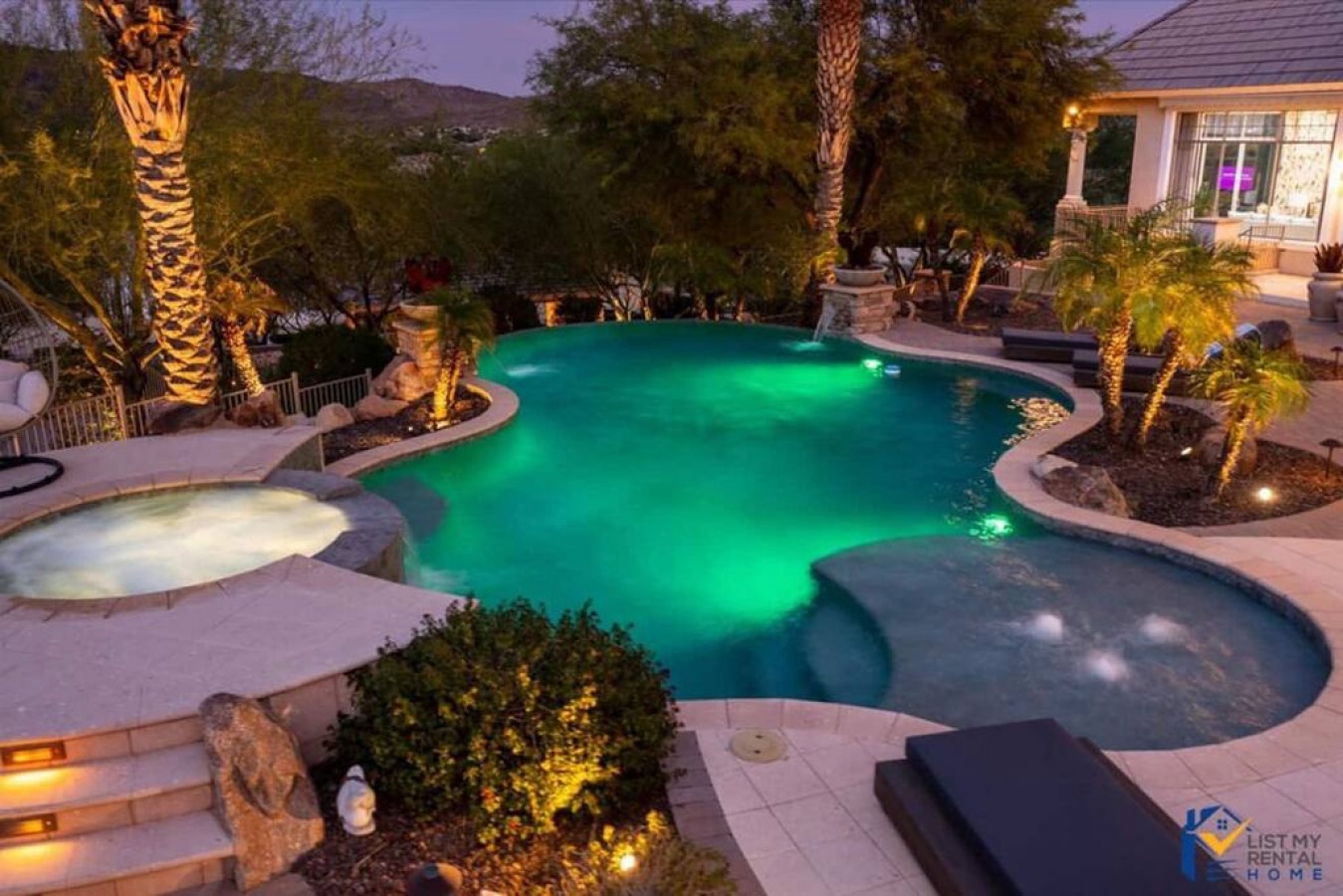 Stunning resort-style pool with emerald lighting creates magical evening ambiance surrounded by palm trees and mountain views.