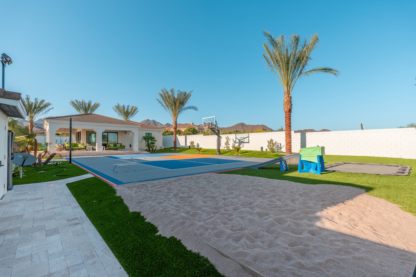 A spacious private estate with full basketball court, manicured lawns, and towering palms, set against mountain views and clear desert skies.