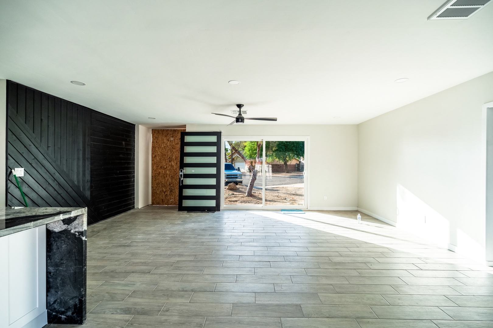 Bright, open living space with stylish wood-look tile floors, modern ceiling fan, and large windows inviting natural light throughout your stay.