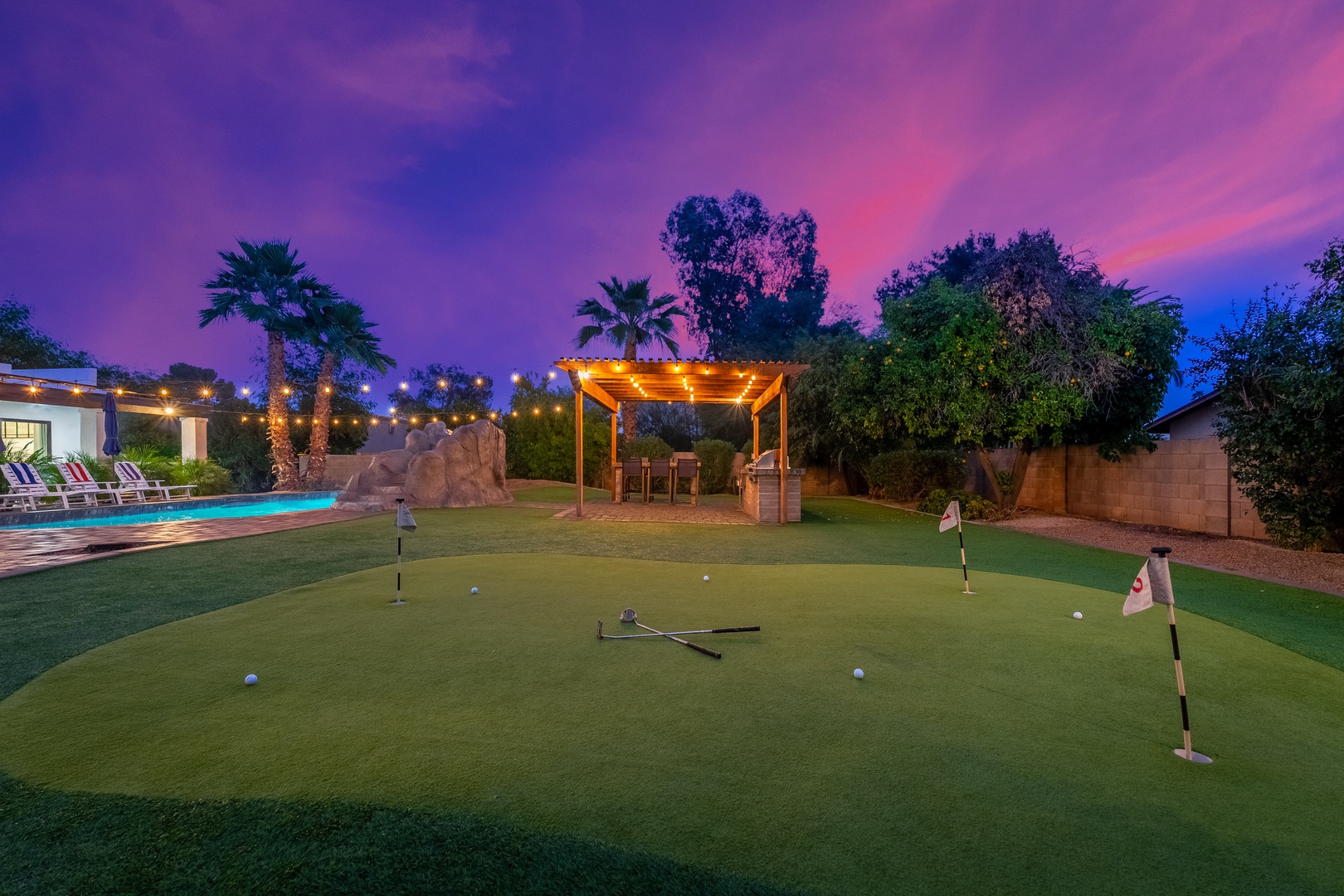 A private putting green awaits under desert twilight, complete with dining pergola, sparkling pool, and tropical palms—an entertainer's paradise.