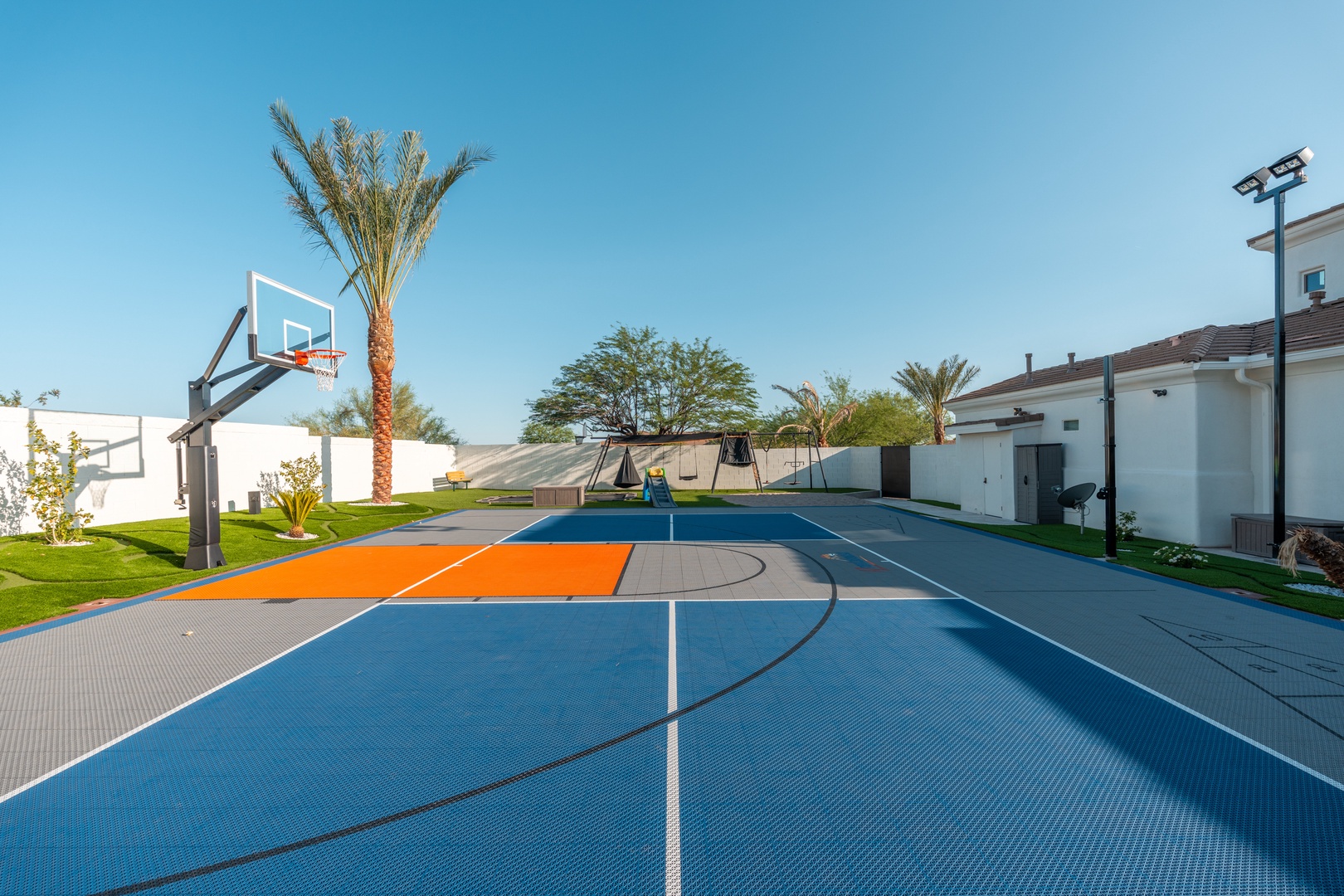 A vibrant outdoor basketball court awaits, complete with professional hoops and colorful surfacing, set against desert palms and lush lawn—perfect for friendly games under sunny skies.