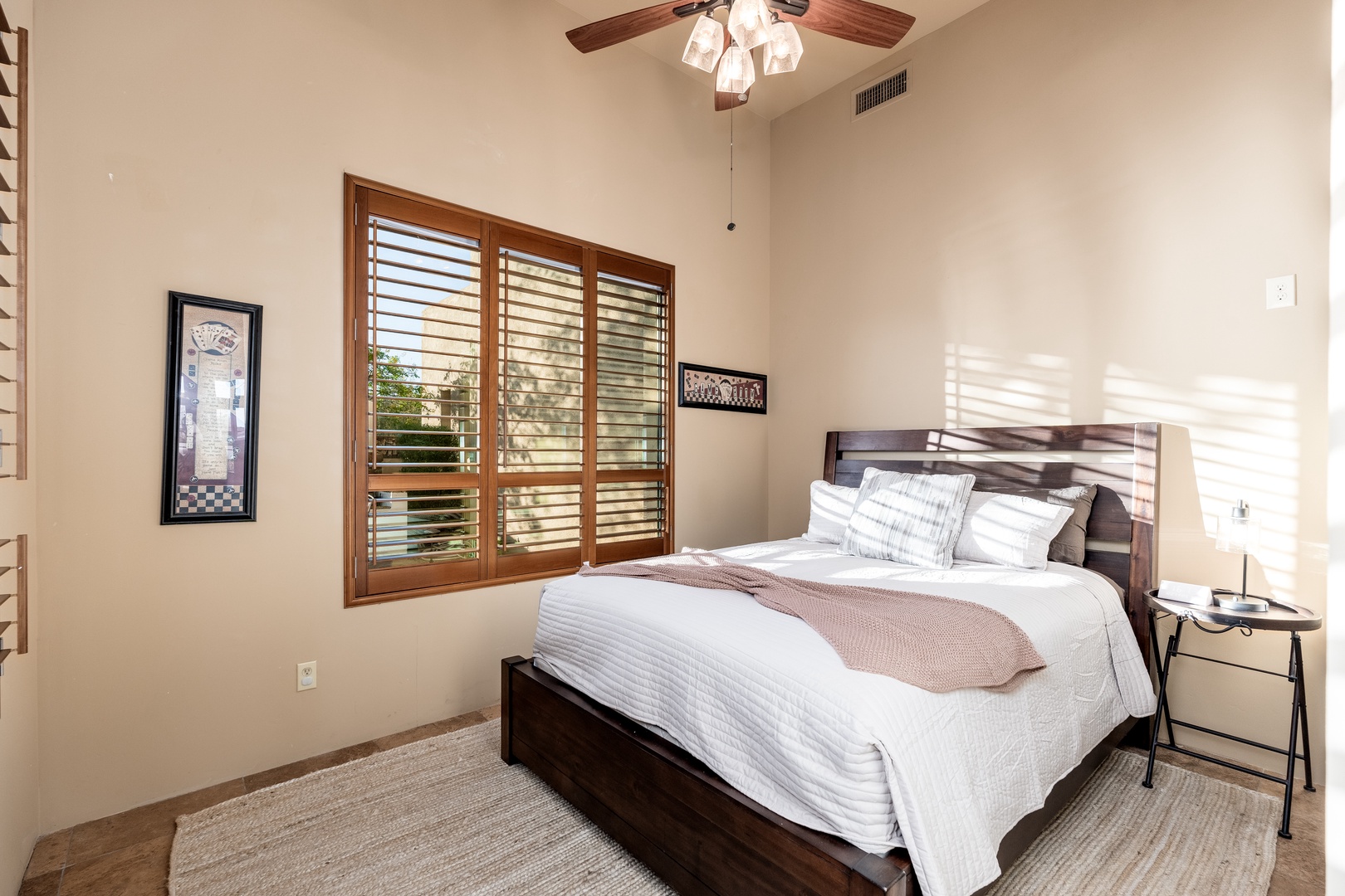 Relax in your serene bedroom with vaulted ceilings, soft natural light filtering through plantation shutters, and a plush bed ready for a restful night's sleep.