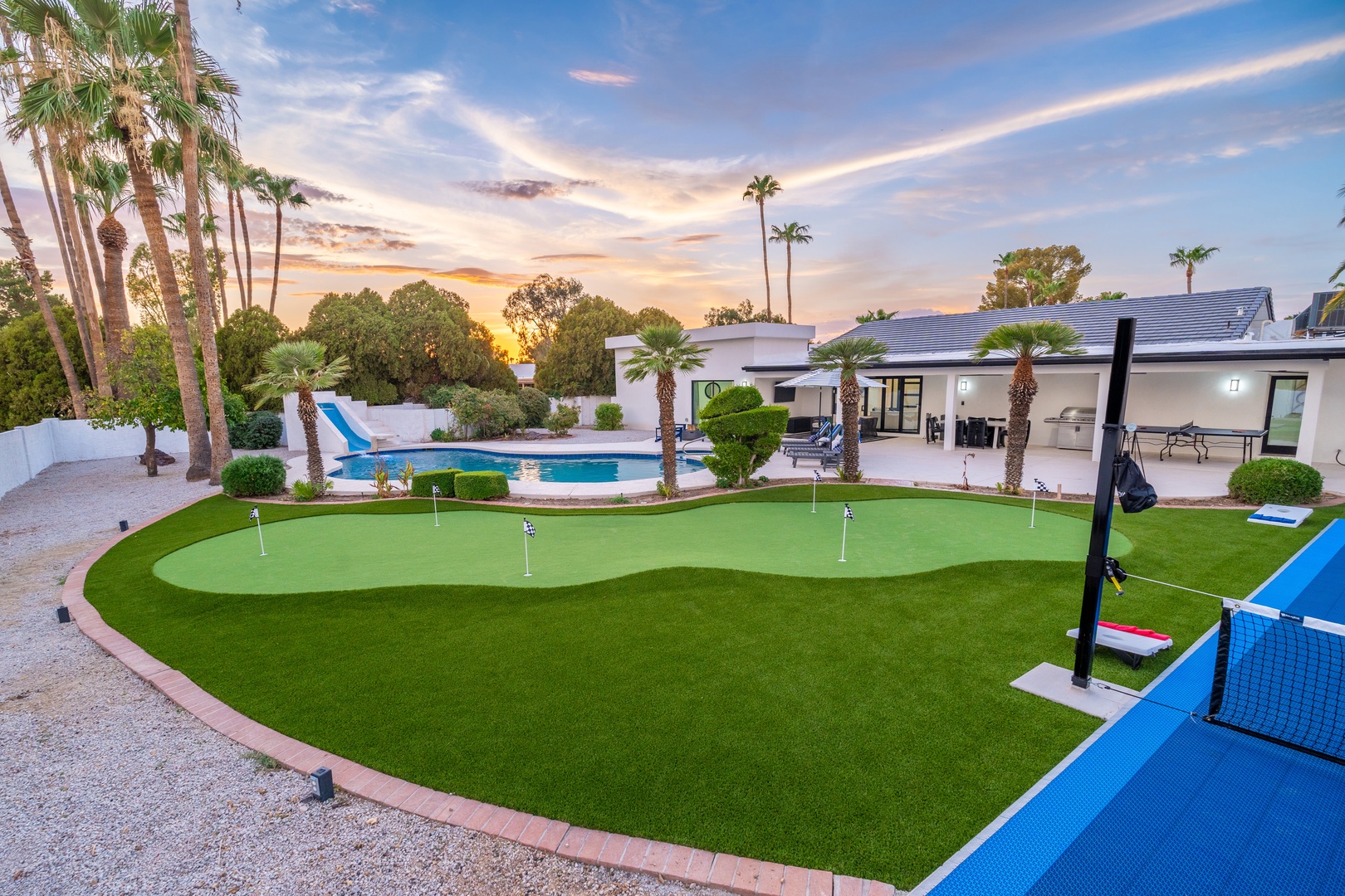 A modern desert retreat with private pool, putting green, and sport court surrounded by manicured landscaping beneath warm Arizona skies.