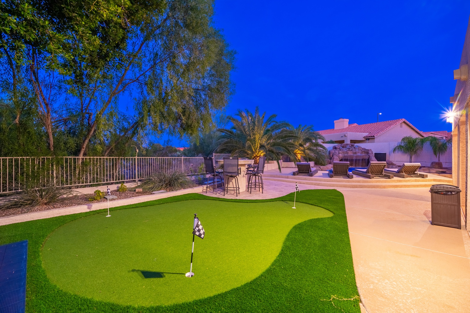 The property features a private backyard putting green with a twilight view, surrounded by palm trees and ample patio seating under a vibrant blue evening sky.