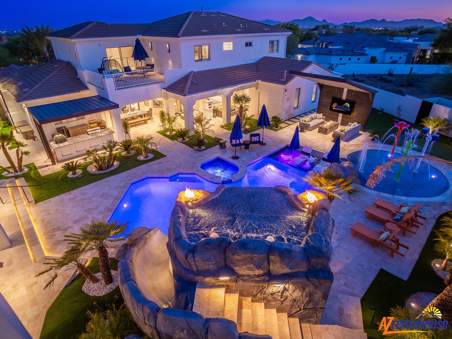 A stunning luxury villa featuring an elaborate pool complex with illuminated blue waters and tropical landscaping at dusk.