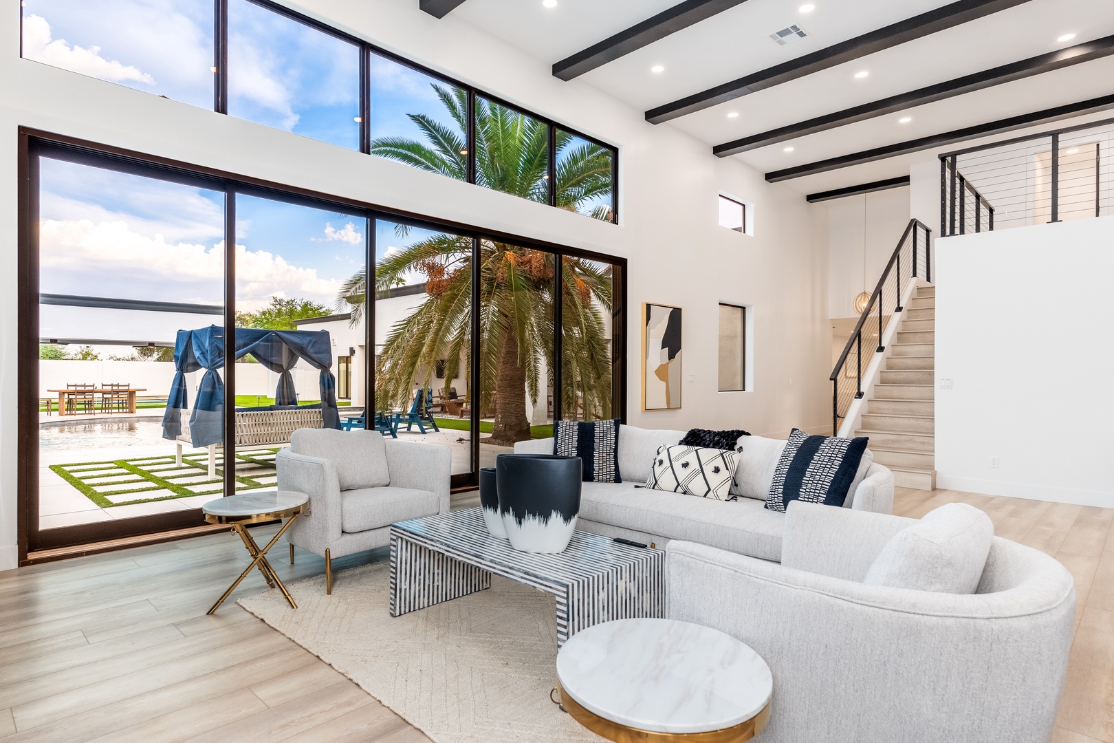 Sink into plush seating and soak in natural light streaming through floor-to-ceiling windows. Elegant beams and art add character, while palm-lined outdoor spaces invite relaxation steps away.