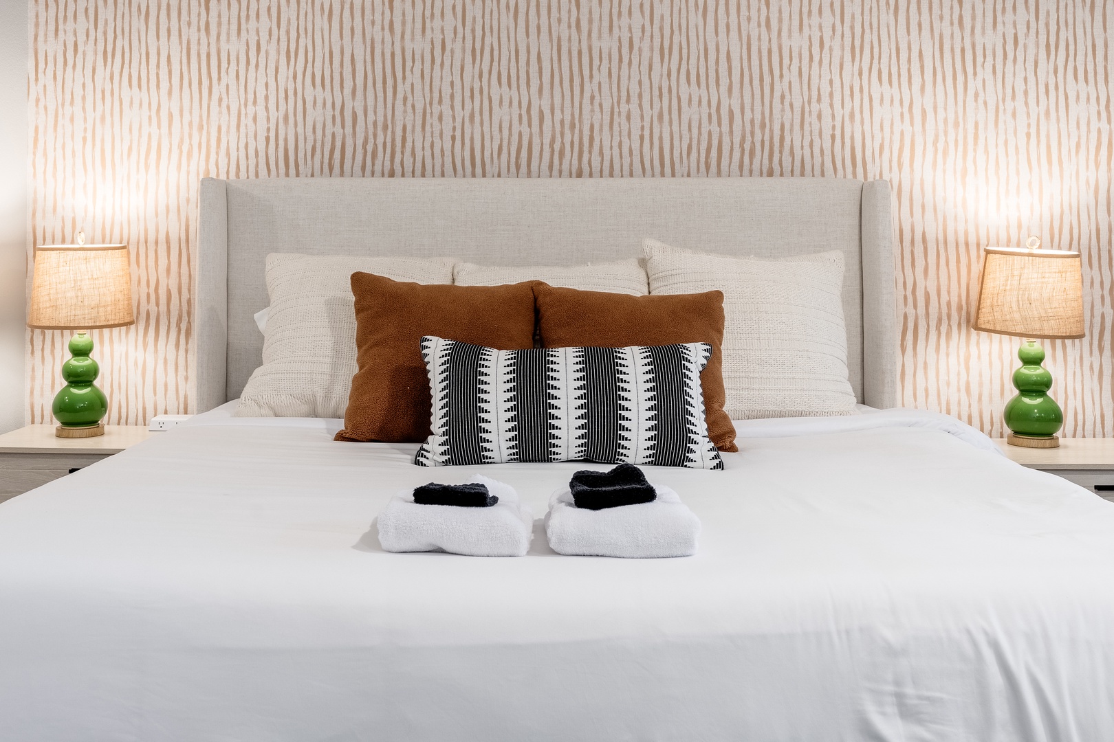 Sink into crisp linens and plush pillows framed by warm lighting and textured walls. Your comfortable retreat awaits with slippers ready at bedside.