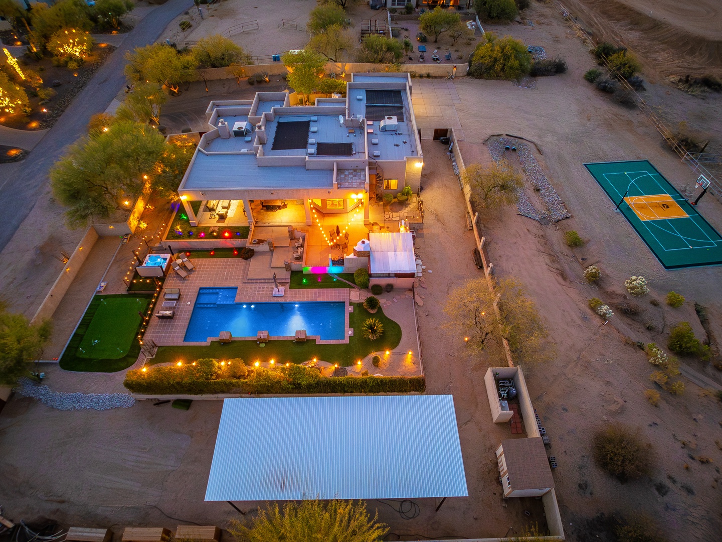 Aerial view capturing a luxury desert retreat with pools, tennis court, outdoor dining, and rooftop terraces—a distinctive property set within natural desert surroundings.