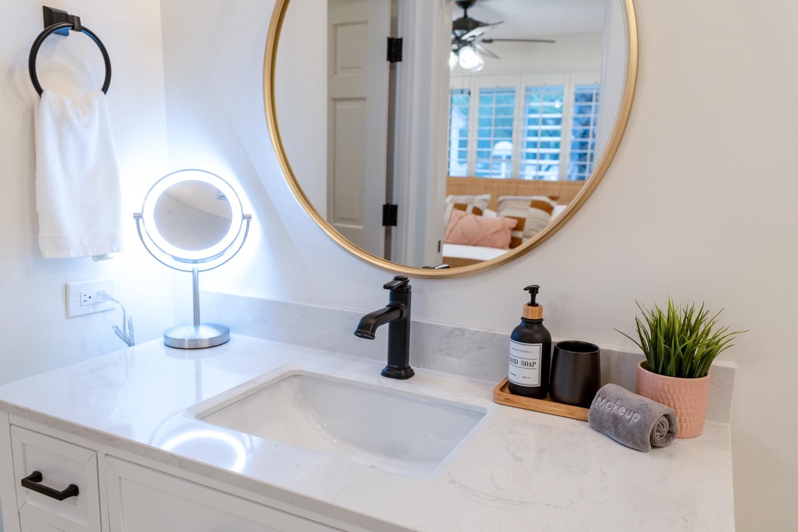 Freshen up in your bright, modern bathroom with elegant marble counters, warm brass mirror, and plush towels ready for you. A peaceful view of your cozy bedroom awaits.