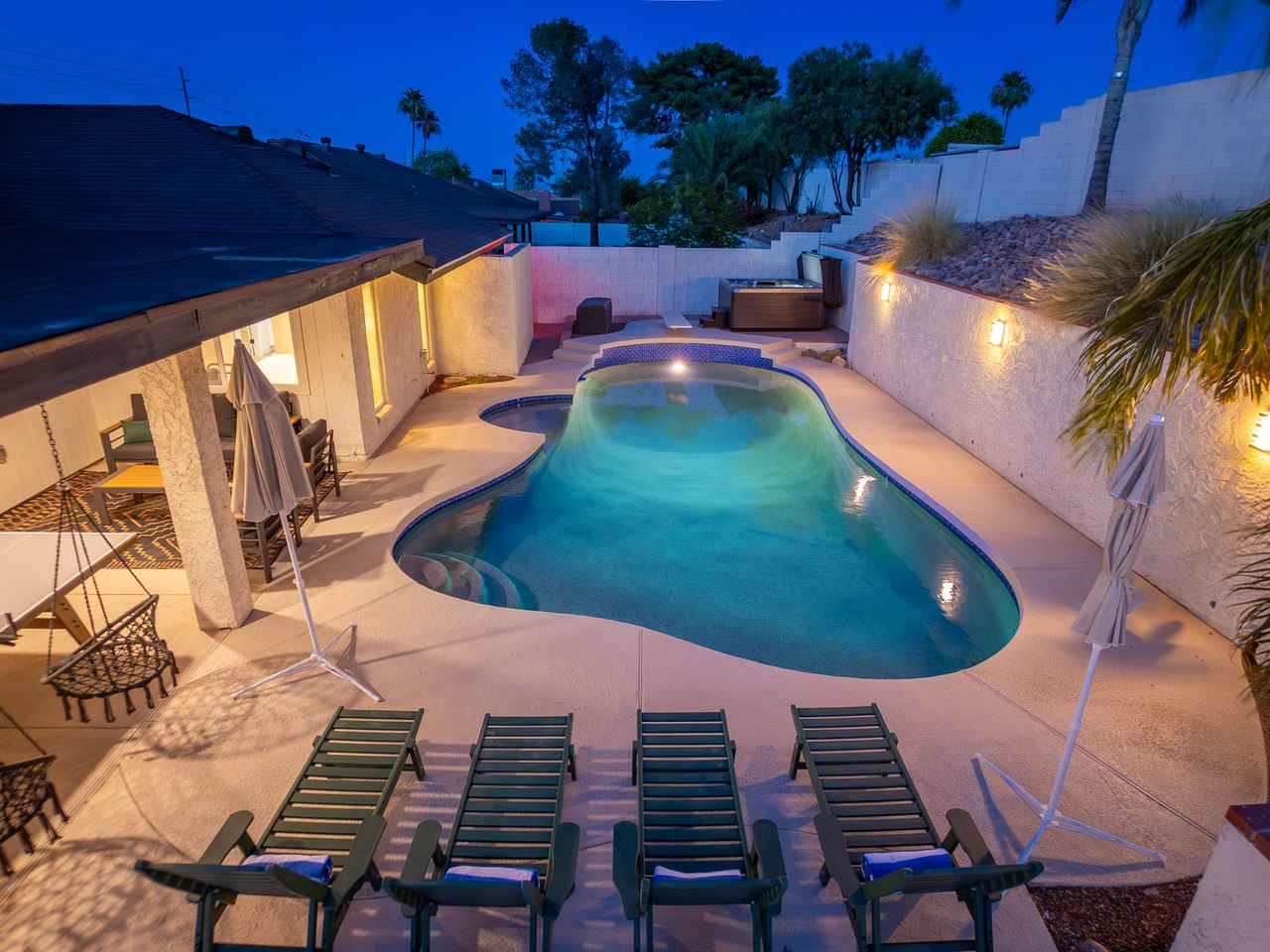 A sparkling private pool awaits you under the evening sky, surrounded by lounge chairs, ambient lighting, and a spa—perfect for unwinding after exploring the area.