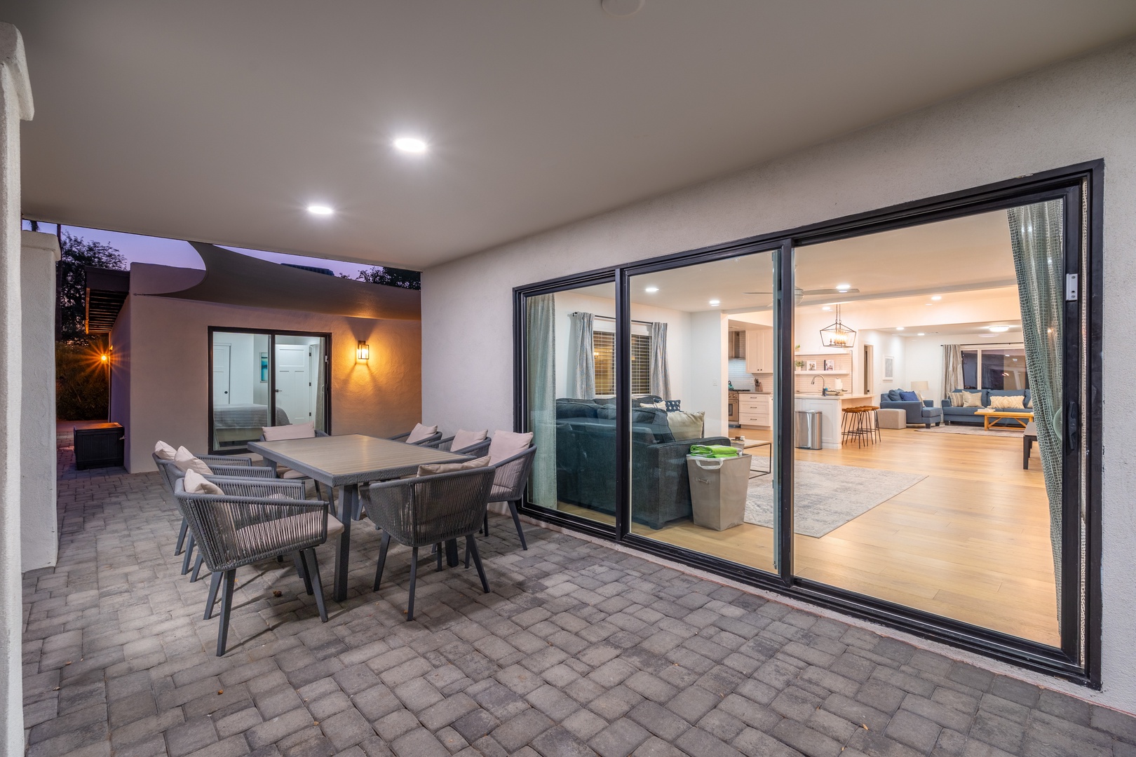 Step onto your private patio, featuring modern outdoor dining under a covered ceiling. Large glass doors invite you into the bright, stylish living area, blending indoor and outdoor living seamlessly for your perfect evening retreat.