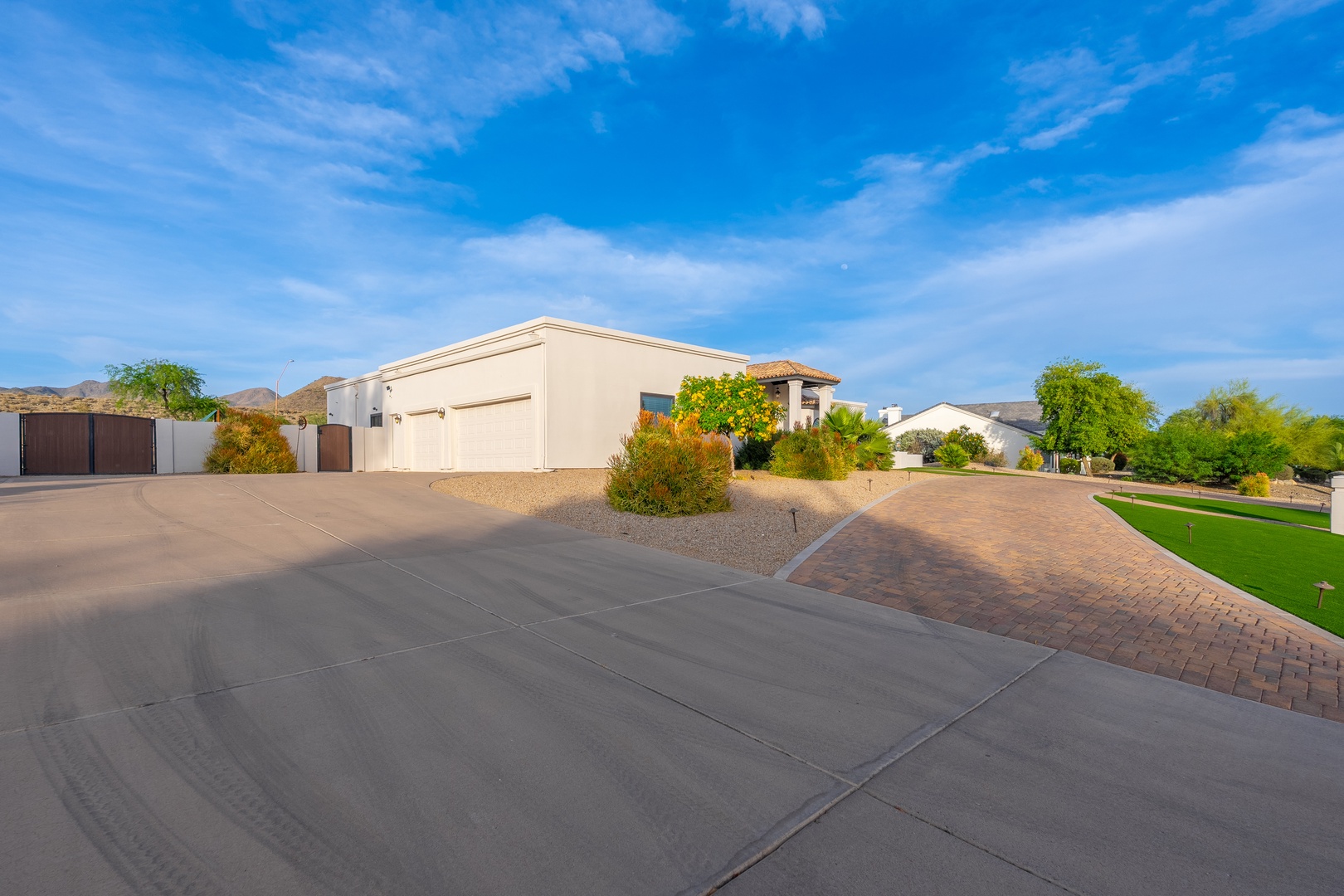 Modern desert home featuring spacious driveway and charming brick-paved walkway, set in a tranquil residential neighborhood with mountain vistas and mature desert landscaping.