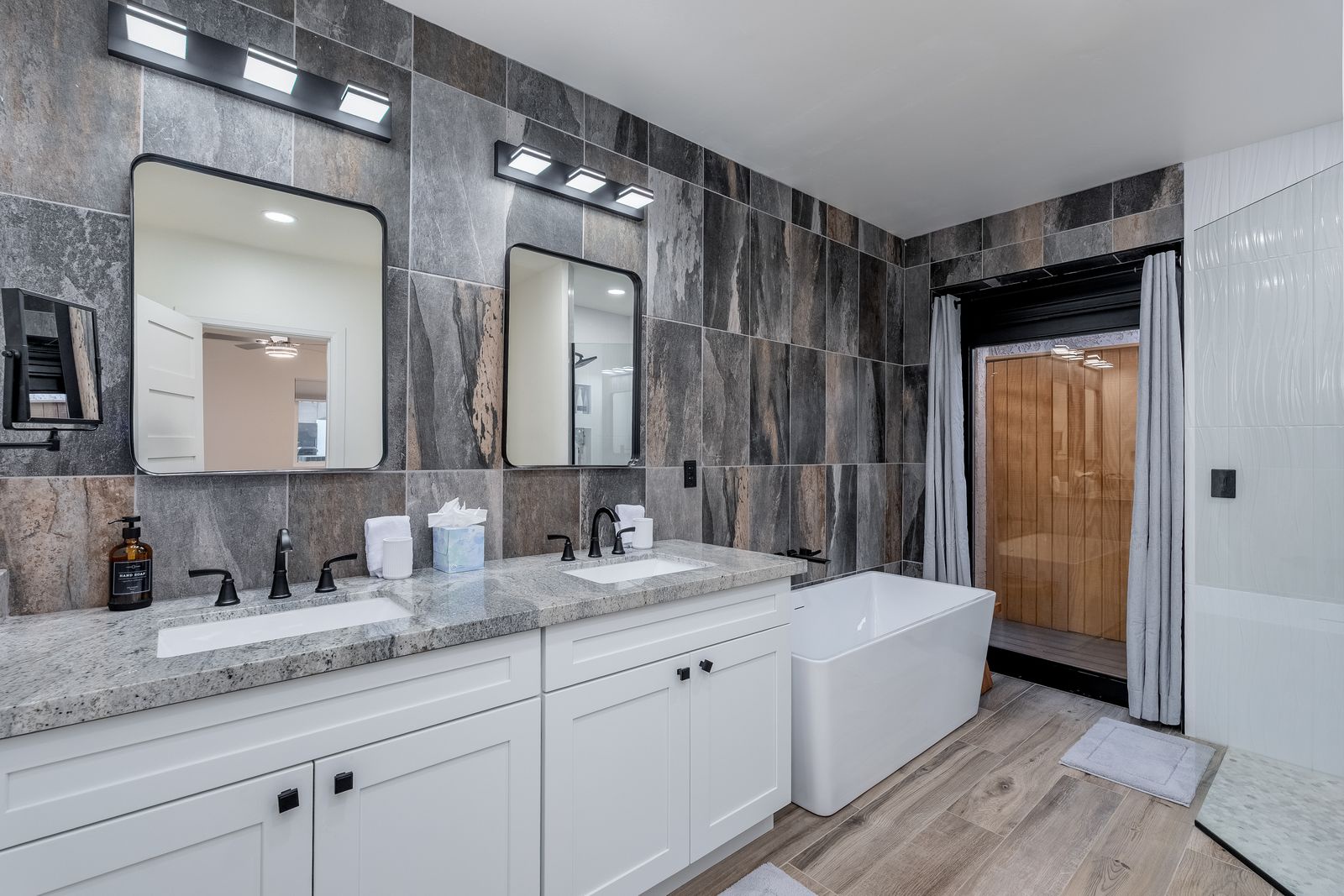 Luxurious spa-like bathroom featuring dual vanities, a soaking tub, and modern finishes. Unwind in elegant comfort with designer lighting, rustic tile accents, and a spacious walk-in shower with privacy curtain.