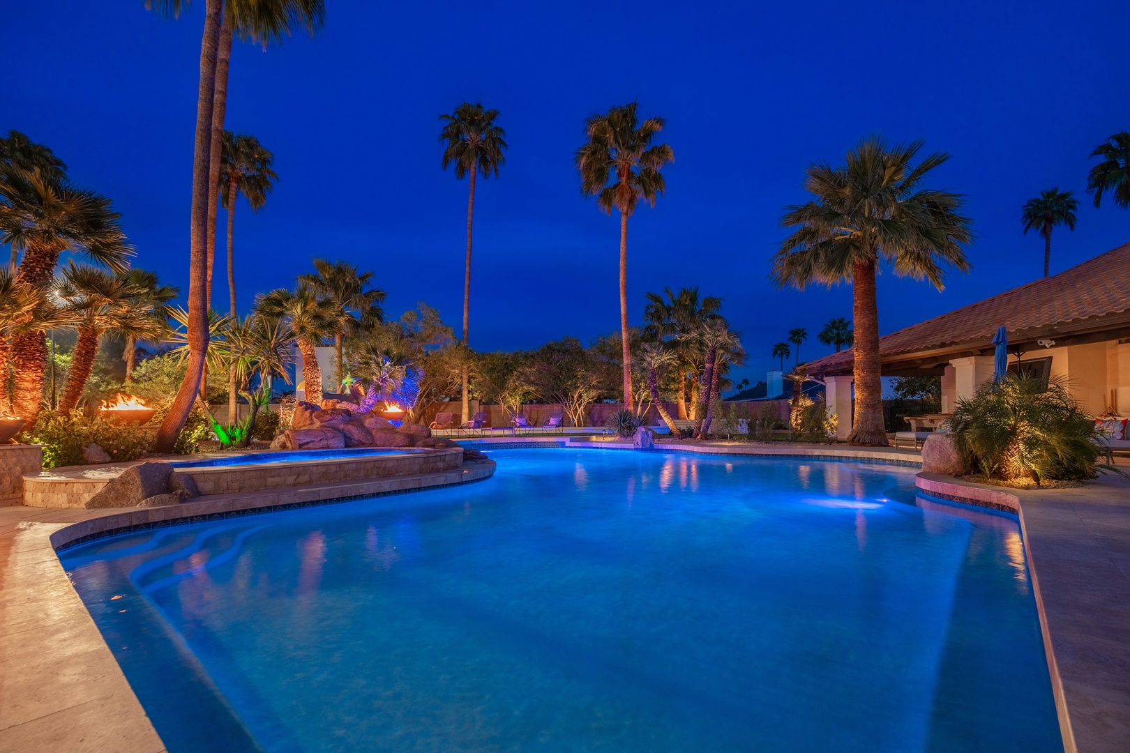 Picture yourself in this stunning desert oasis at twilight, where palm trees tower above illuminated pools glowing in serene blue. Your private paradise awaits under the evening sky.