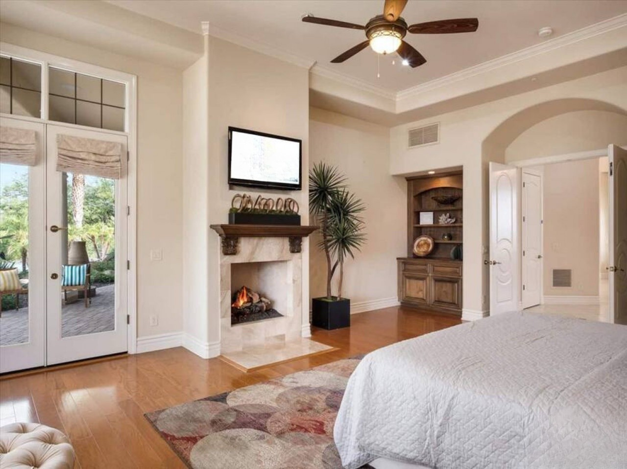 Step into your luxurious primary suite with gleaming hardwood floors, a cozy fireplace, and French doors opening to a private patio—your perfect retreat.