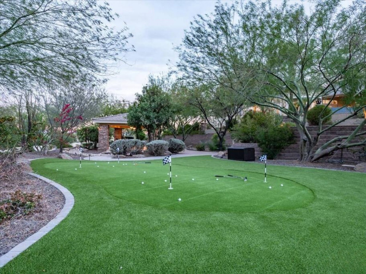 Private putting green surrounded by mature desert landscaping and views of the contemporary property entrance—a unique outdoor recreational space for your stay.