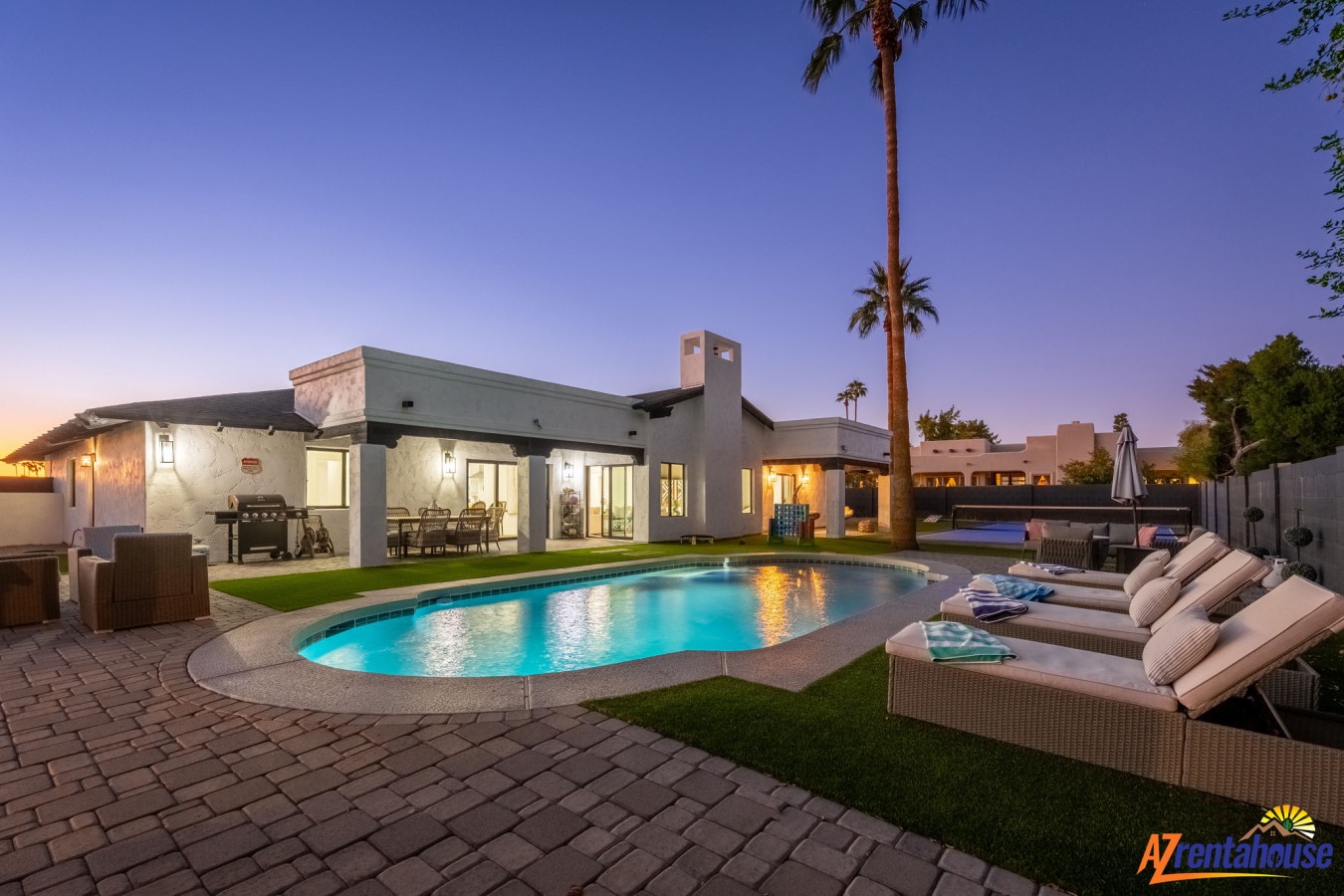 Modern desert retreat featuring a sparkling pool surrounded by palm trees and manicured lawn at twilight.
