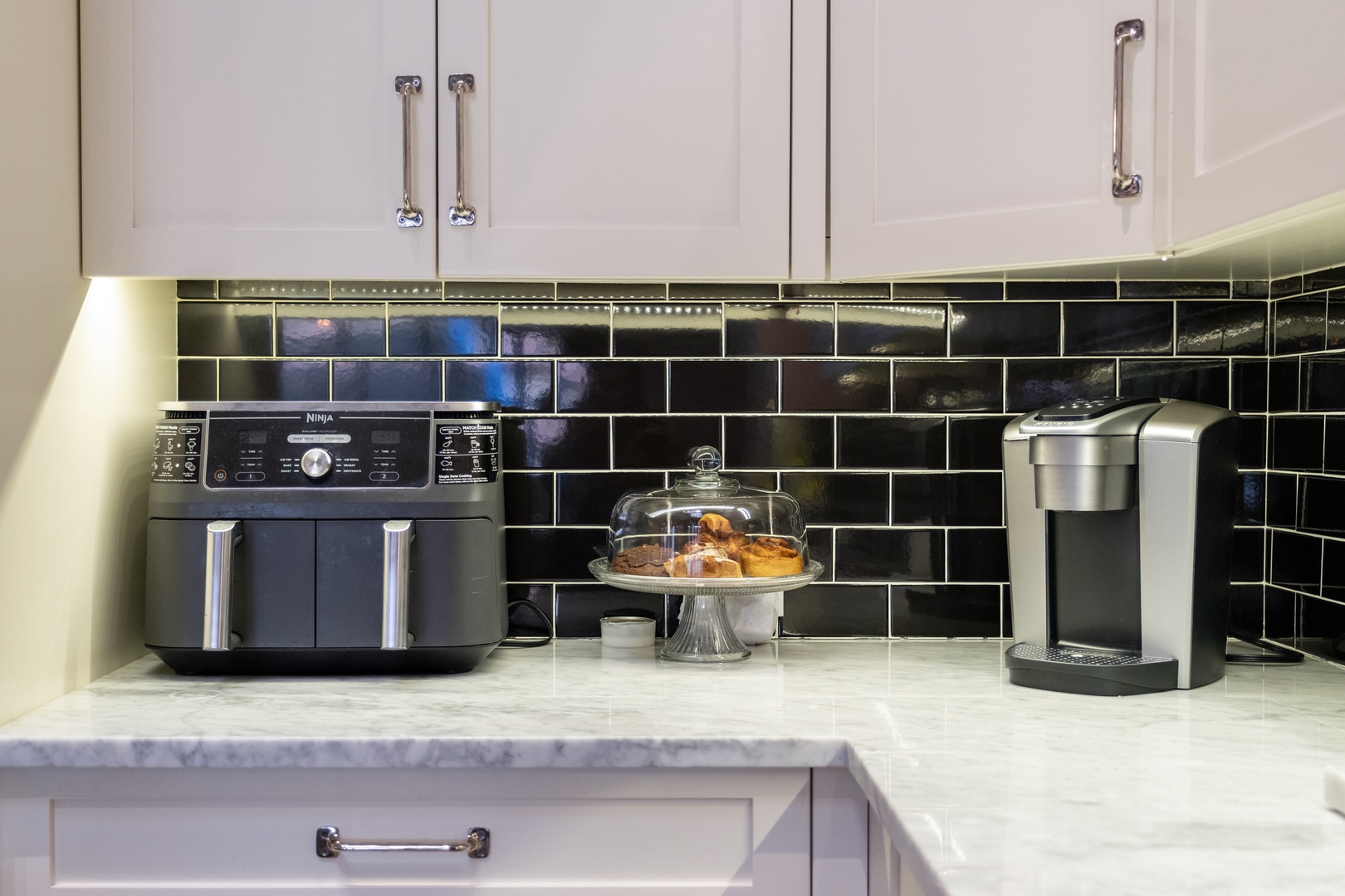 Your modern kitchen features sleek white cabinetry, stylish black tile backsplash, and marble countertops ready for your morning coffee ritual.