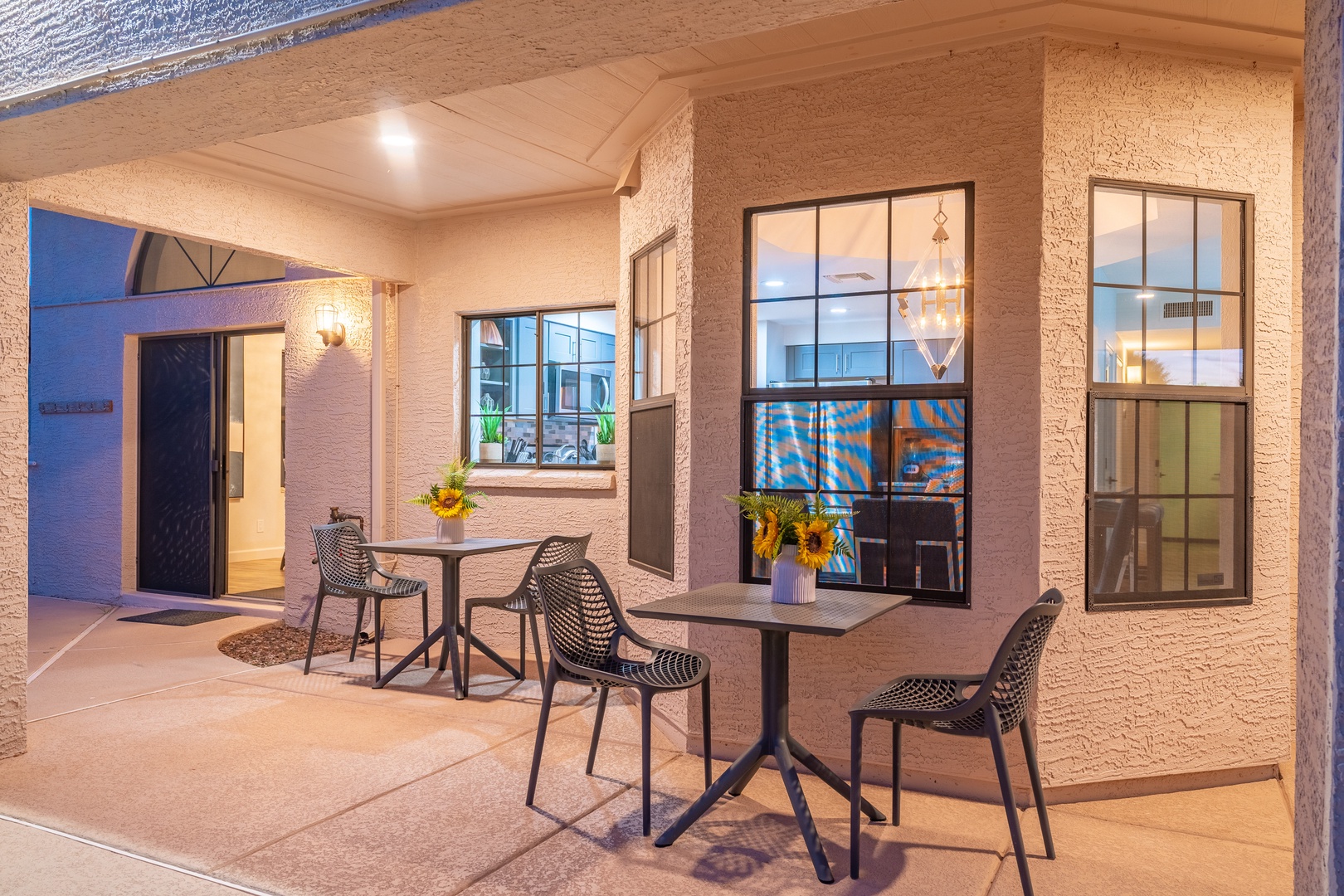 A welcoming entrance courtyard where you can relax at sunset, with charming bistro seating and warm windows glowing behind, setting a tranquil tone for your stay.