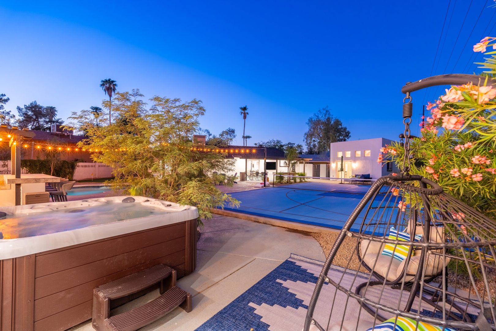 Spacious backyard oasis featuring a sparkling pool, relaxing hot tub, and covered patio with twinkling lights—your perfect retreat for unwinding under warm evening skies.