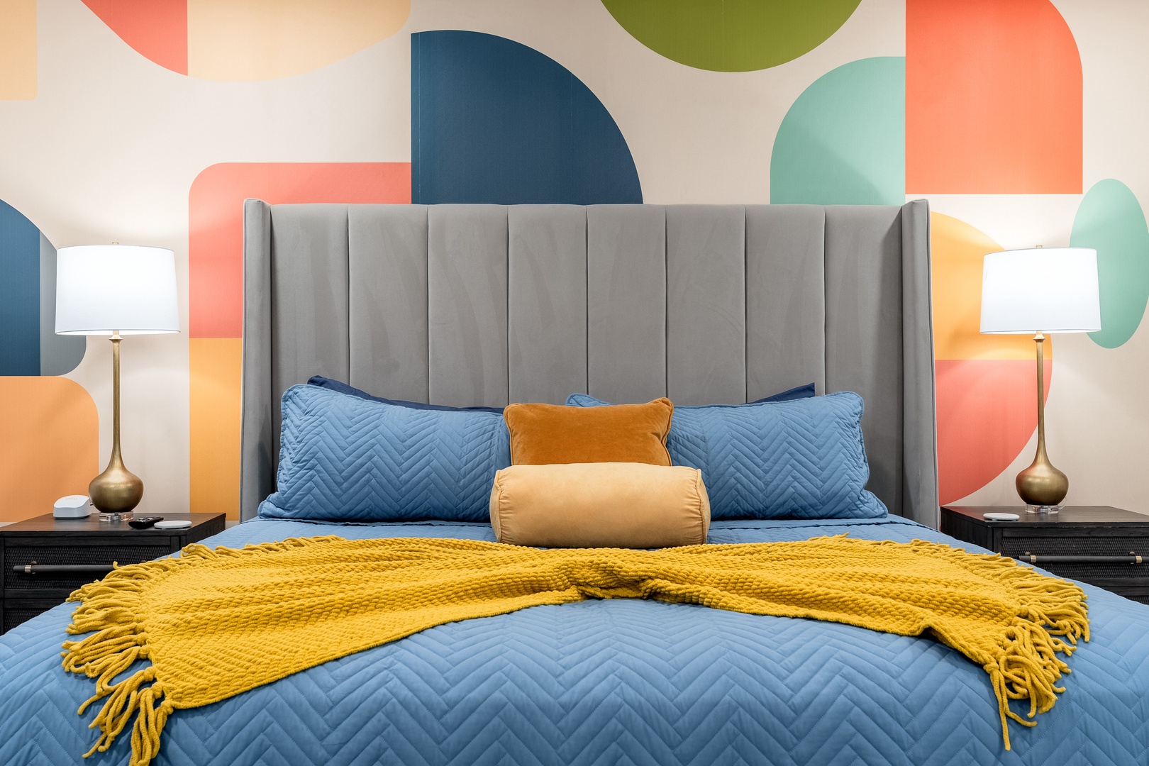 Settle into your plush bed surrounded by vibrant geometric art and soft lighting. The cozy throw and layered pillows invite you to unwind in this cheerful, modern retreat.