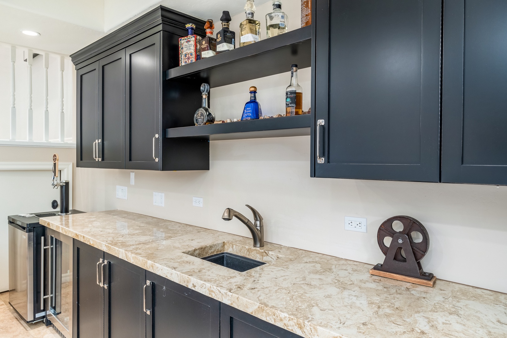 Your private wet bar features sleek navy cabinetry, elegant stone countertops, a beverage cooler, and open shelving for your favorite drinks and glassware.