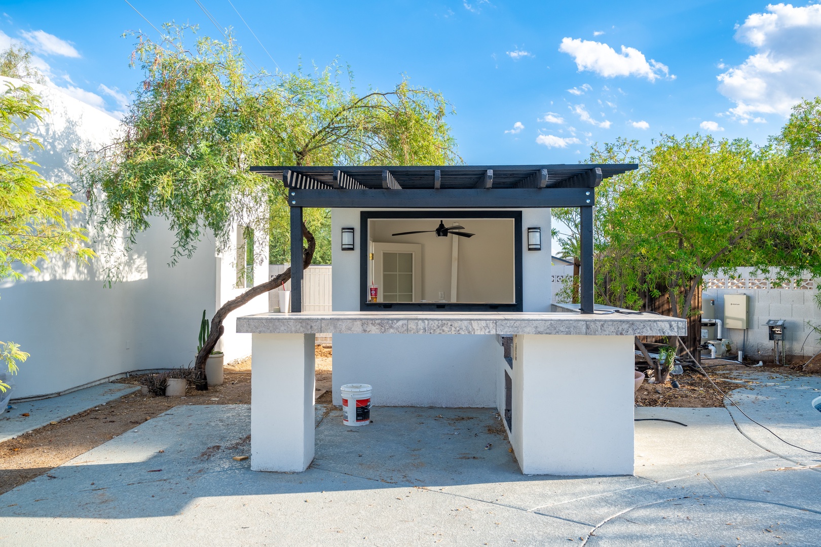 Modern outdoor pavilion with pergola and counter seating, set against lush greenery and blue skies, providing an ideal spot for al fresco dining.