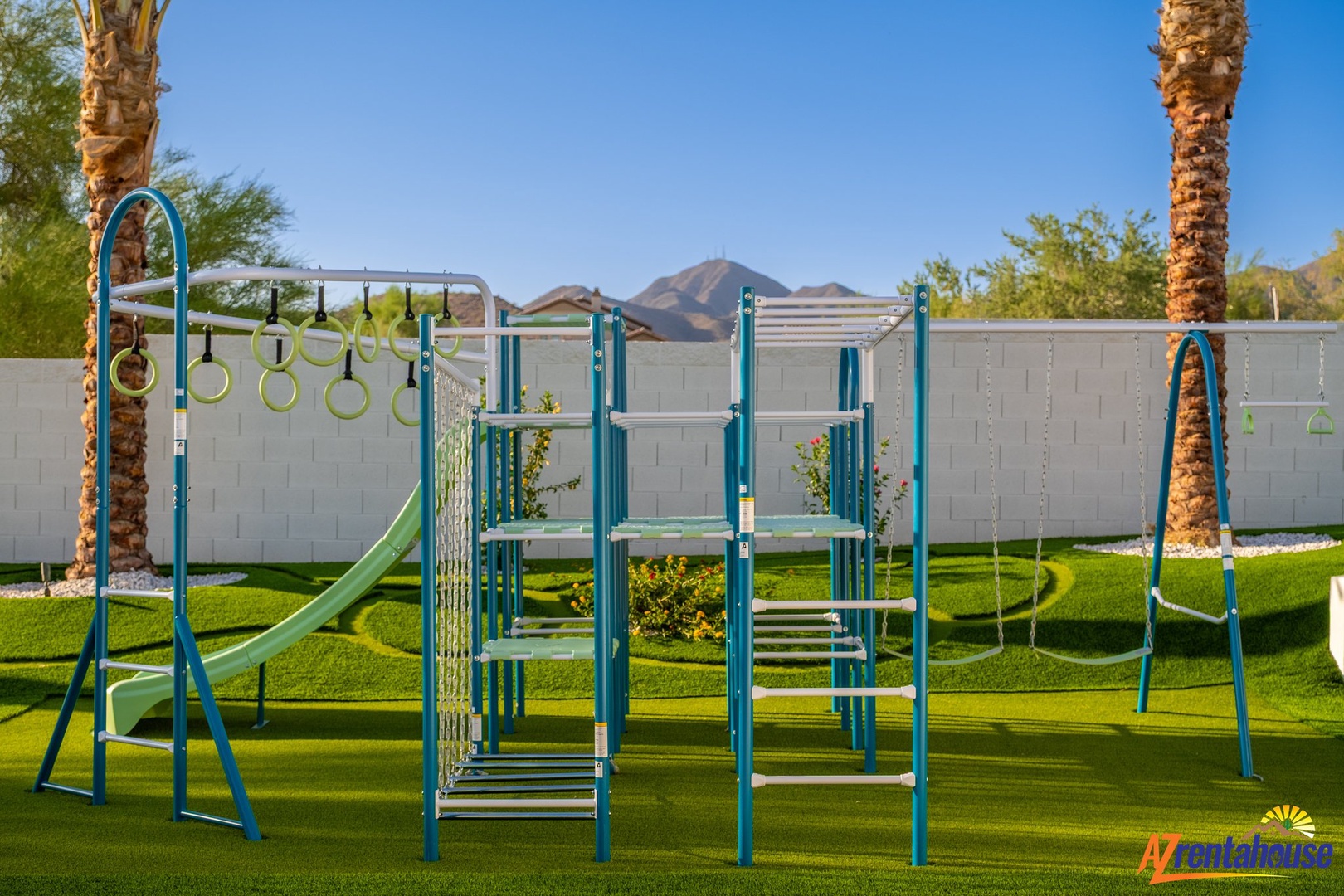 Modern playground with slides, climbing equipment and swings set on manicured lawn with mountain backdrop.