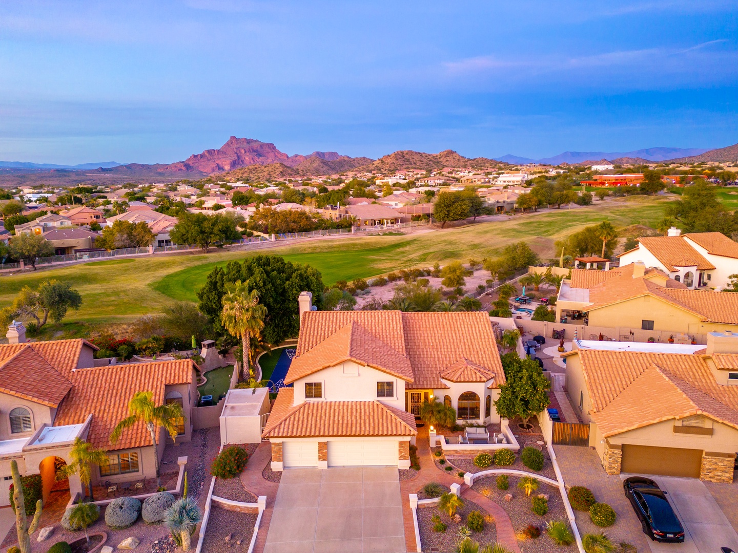 Aerial view showcasing the property nestled in a scenic desert community, with dramatic mountain ridges and a nearby golf course defining the surrounding landscape.