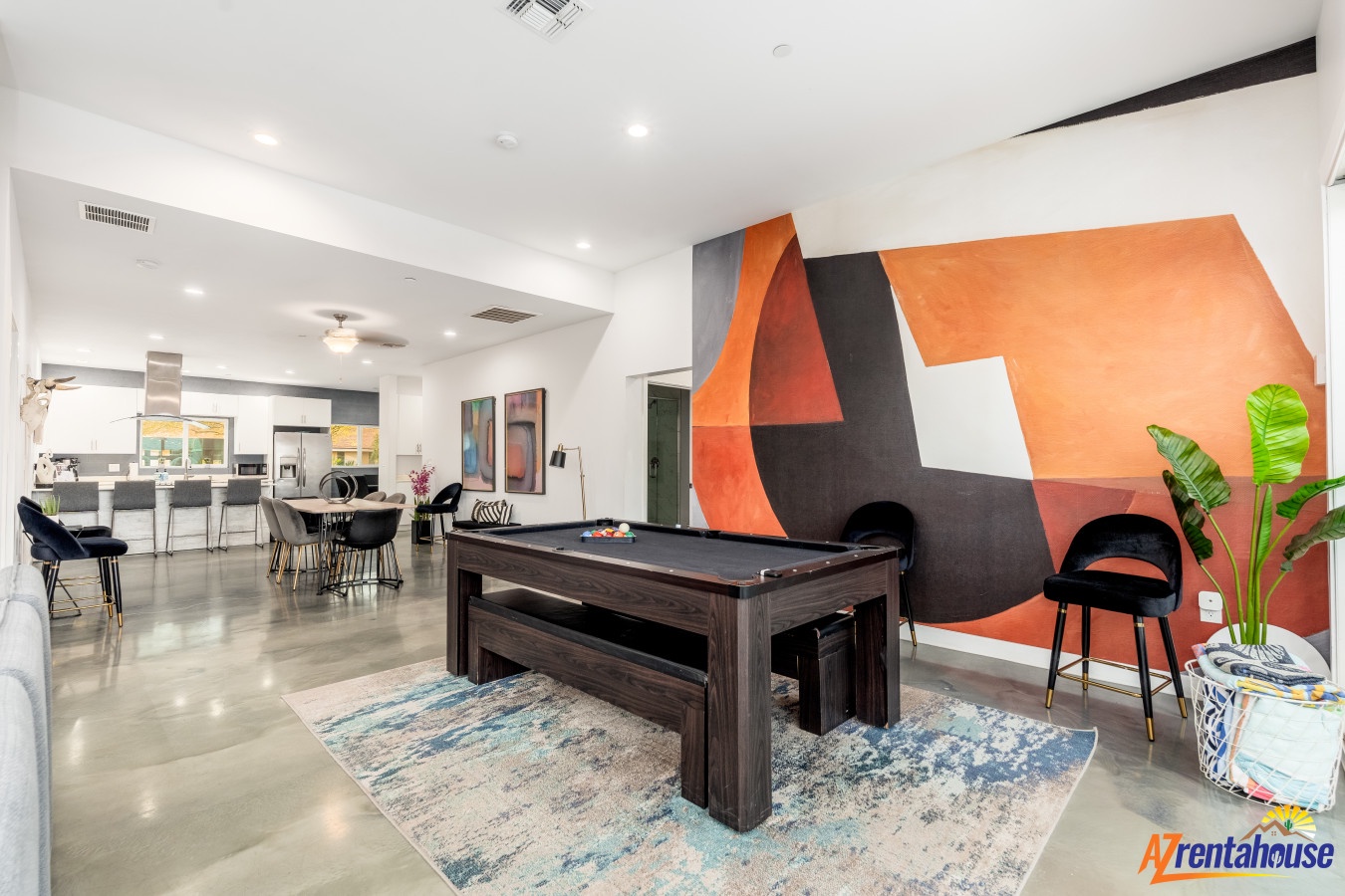 Your stylish game room features a sleek pool table surrounded by vibrant orange geometric wall art and tropical plants for entertainment.