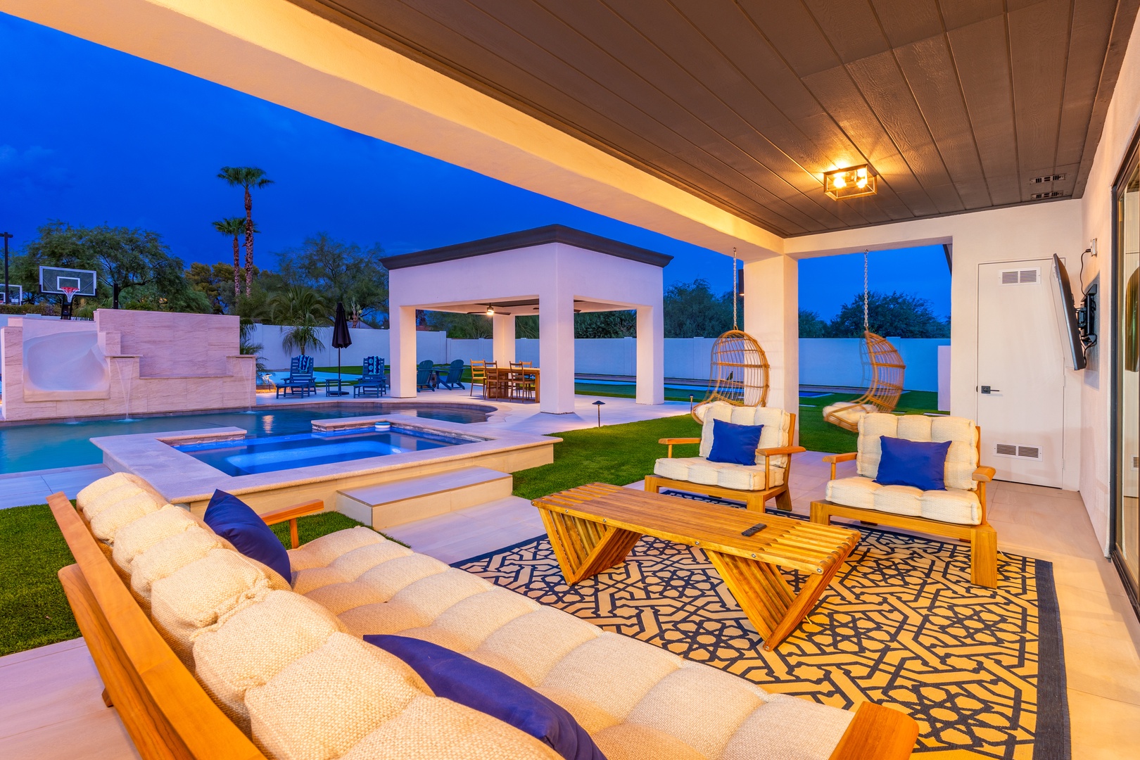 Unwind in your private outdoor oasis, complete with a sparkling pool, cozy seating, and hanging chairs perfect for starlit evenings under a stunning twilight sky.