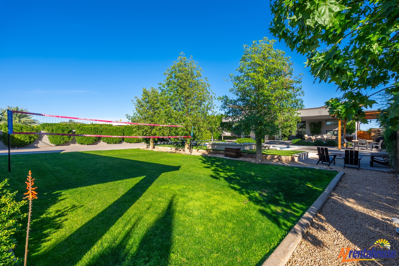 Expansive lawn perfect for games and relaxation, with volleyball net and shaded outdoor dining area ready for your gatherings.