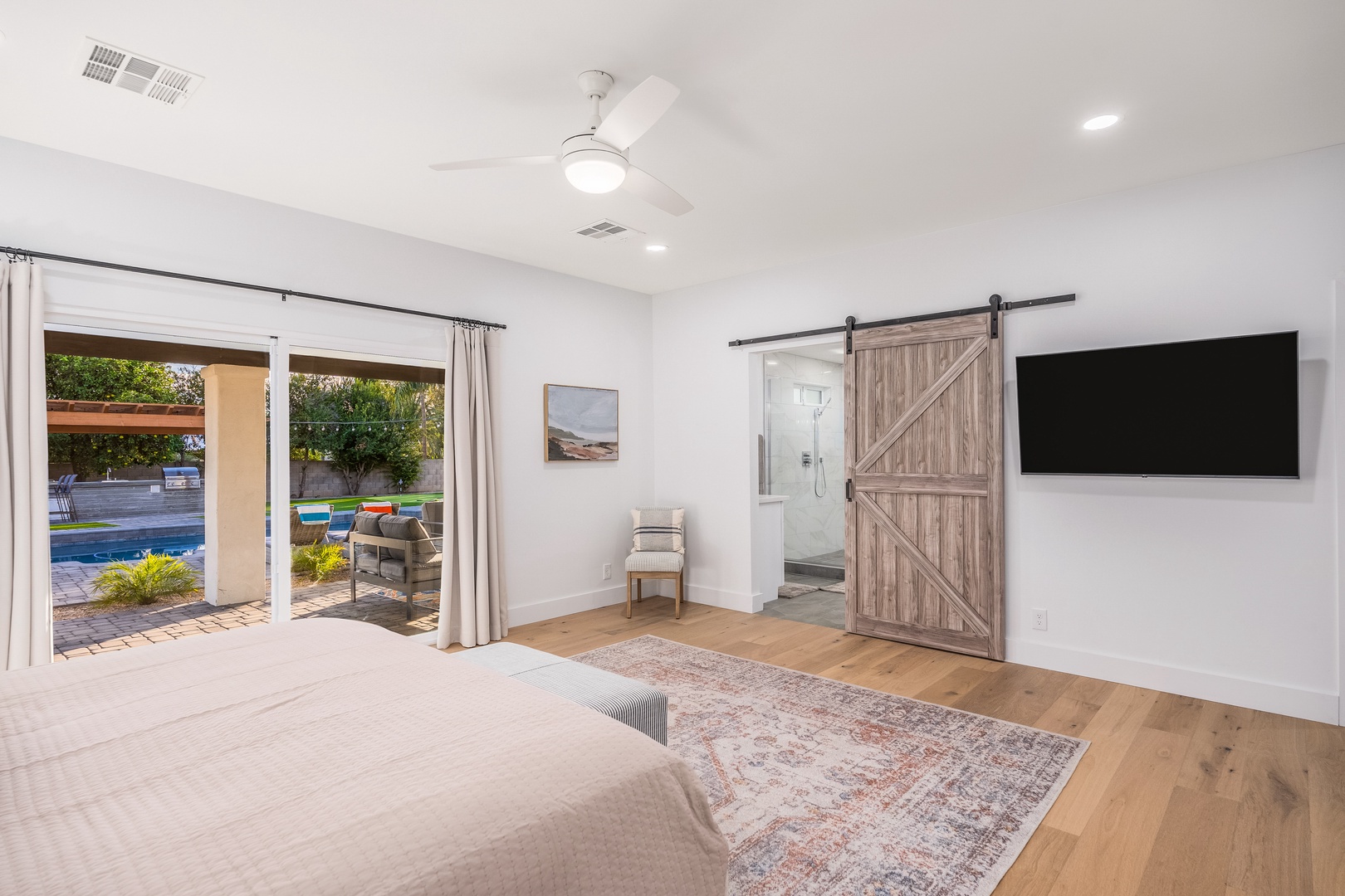 Your serene bedroom features a rustic barn door leading to your private ensuite, while sliding glass doors open to your own backyard oasis—wake to pool views.
