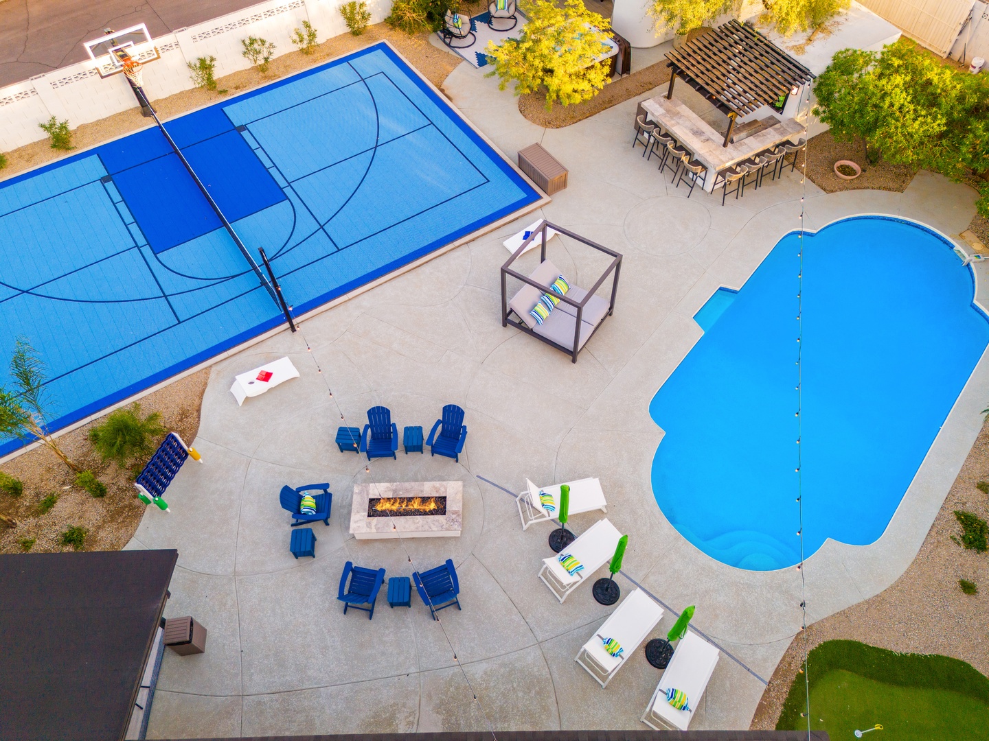 Aerial view of expansive outdoor amenities featuring a sparkling pool, full-size basketball court, fire pit seating area, outdoor dining bar, and manicured landscaping—ideal for group gatherings and active retreats.
