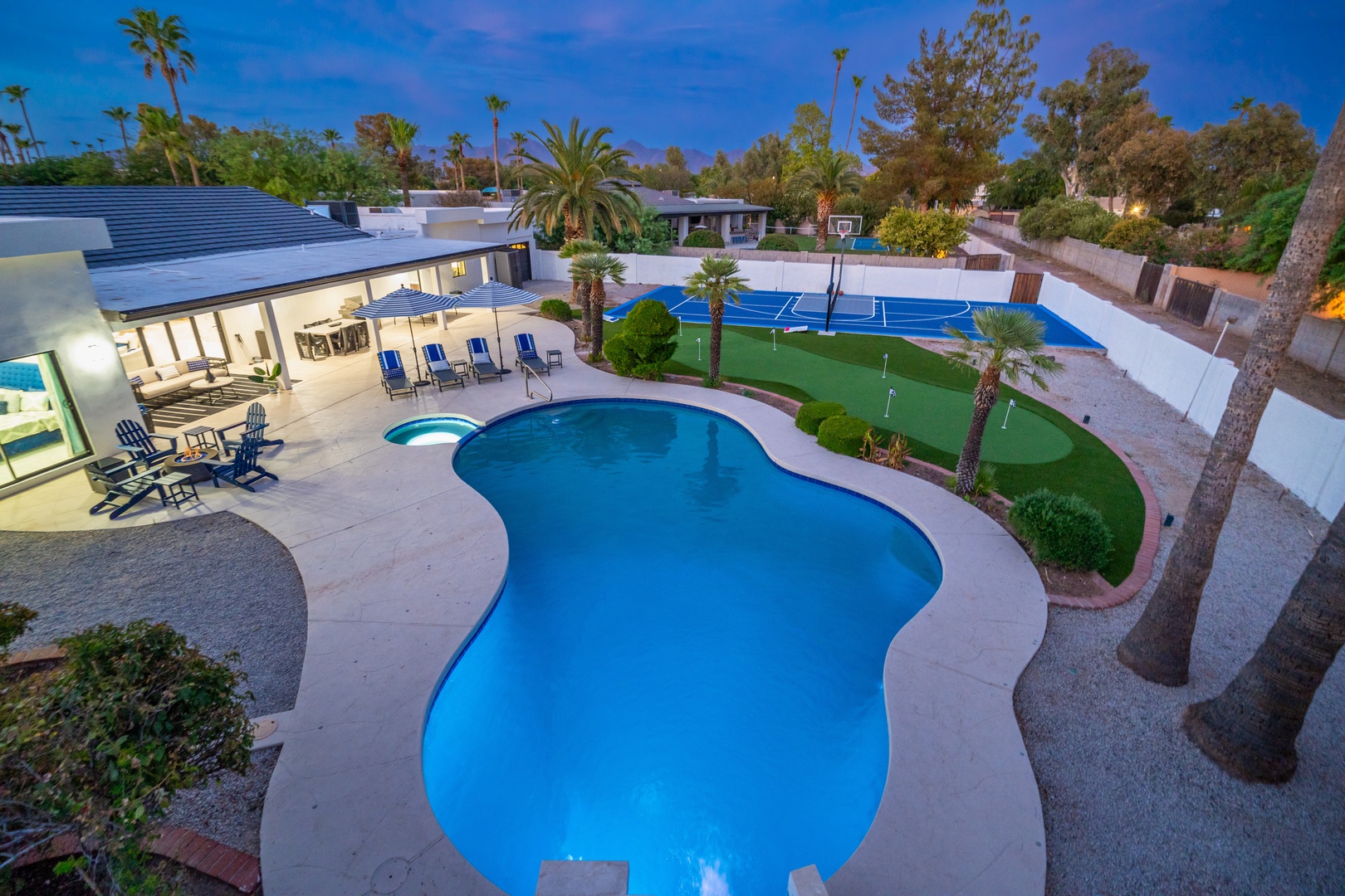 This property features a custom freeform pool, spa, sports court, putting green, and expansive patio surrounded by mature palms and manicured landscaping in a private residential setting.