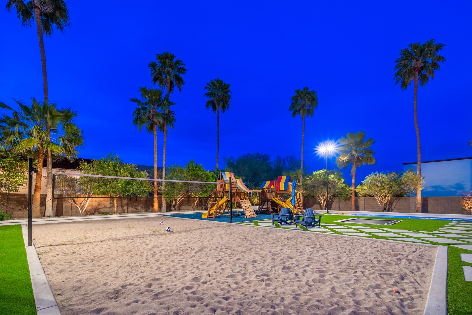 The property features a spacious outdoor play area with a sandy beach zone, colorful playground equipment, and a volleyball court under swaying palms—ideal for family fun.