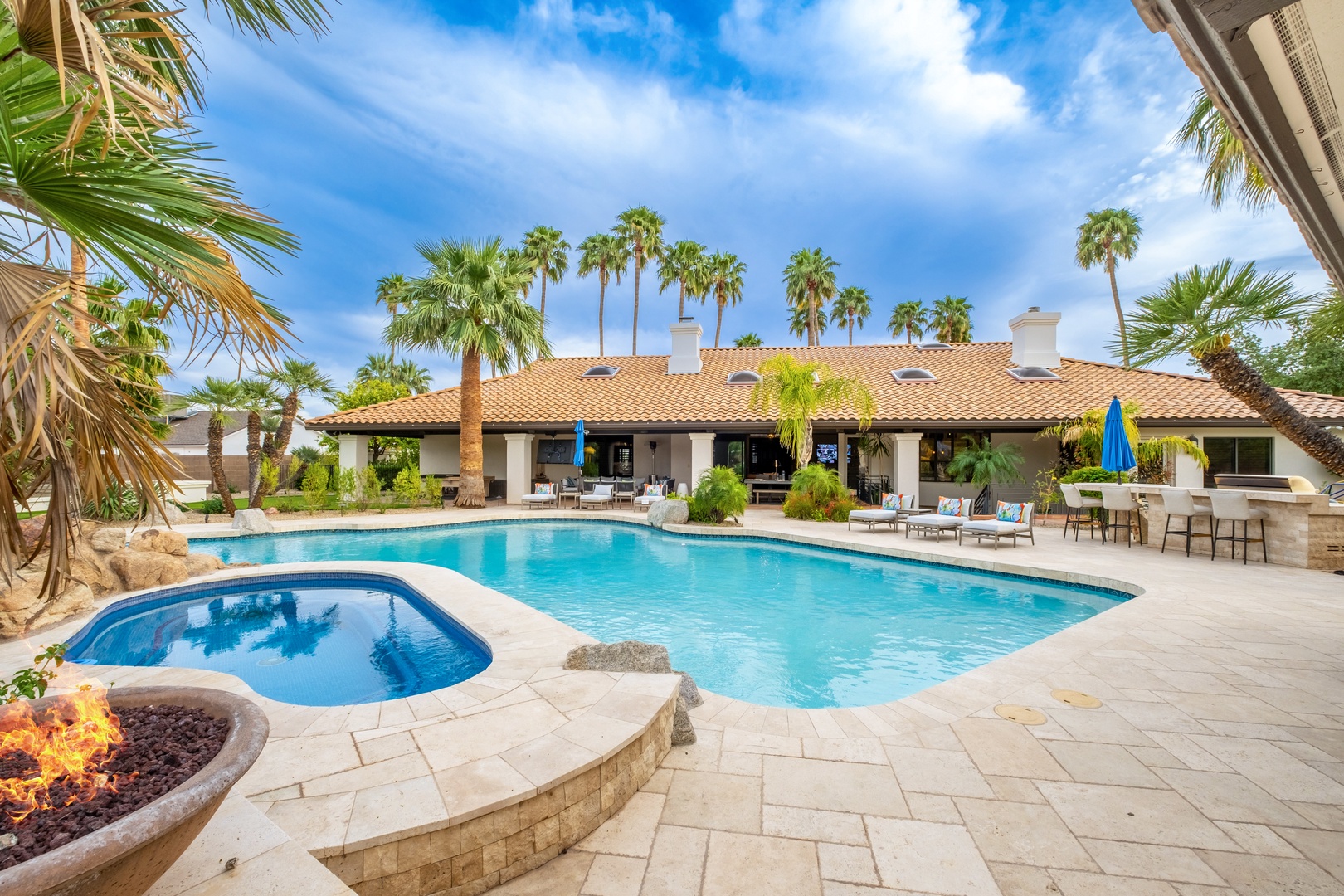 A sprawling resort-style backyard features dual pools surrounded by lush palm trees, spacious covered patios, and poolside lounging areas perfect for entertaining or unwinding.