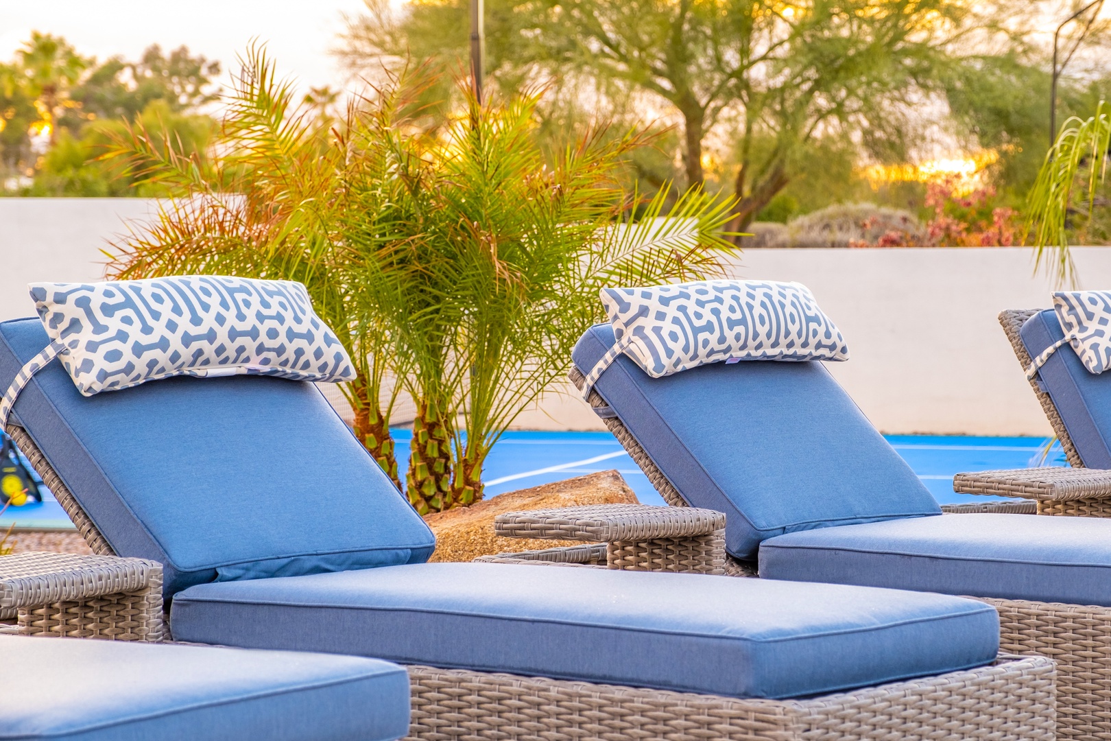 Stylish poolside loungers with plush cushions invite relaxation under swaying palms as the sun dips behind lush tropical gardens.