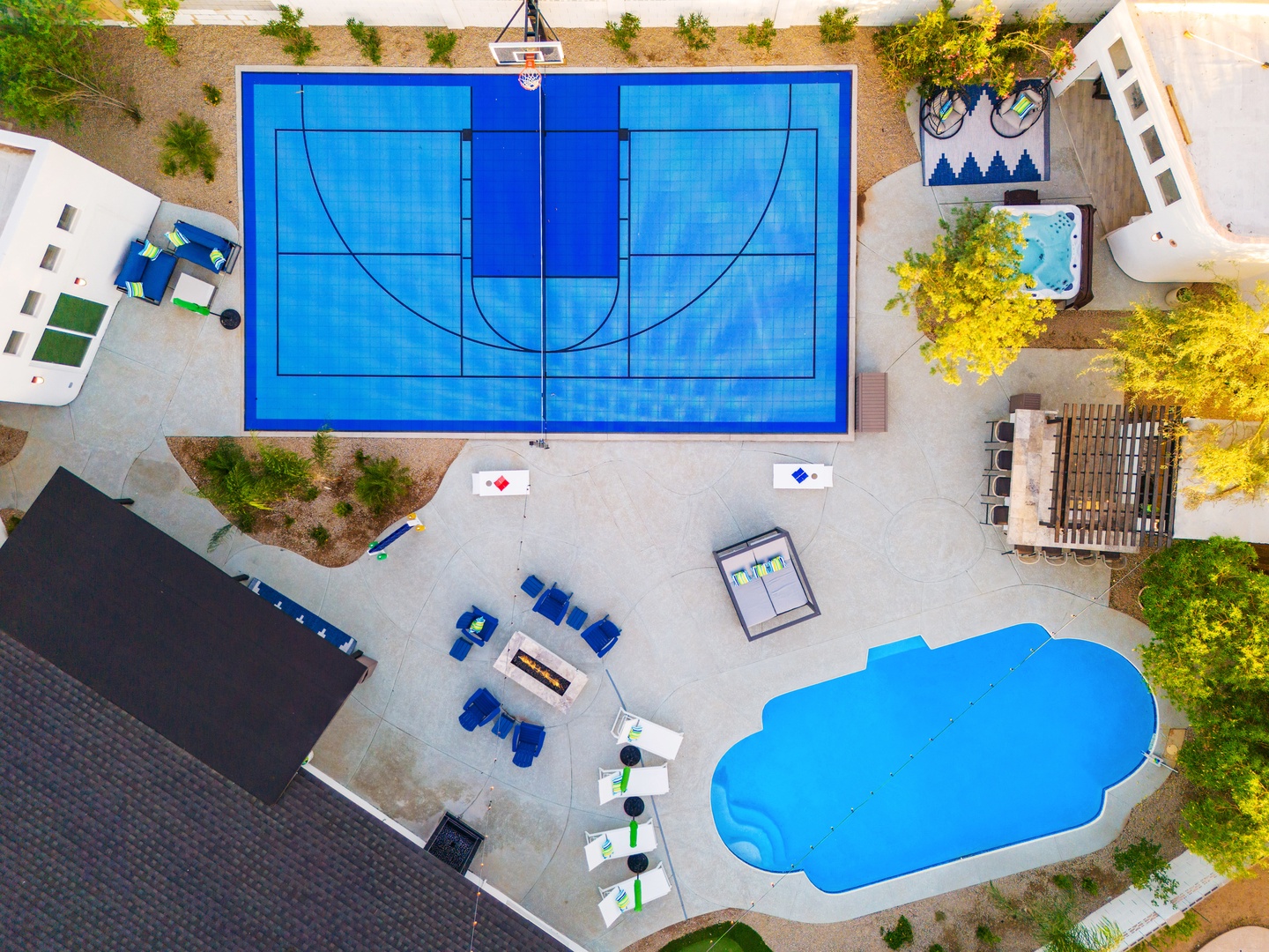 Aerial view showcasing the property's extensive recreational amenities: a regulation basketball court, multiple seating areas, a uniquely shaped pool, and a separate spa, all nestled within landscaped grounds with mature trees.