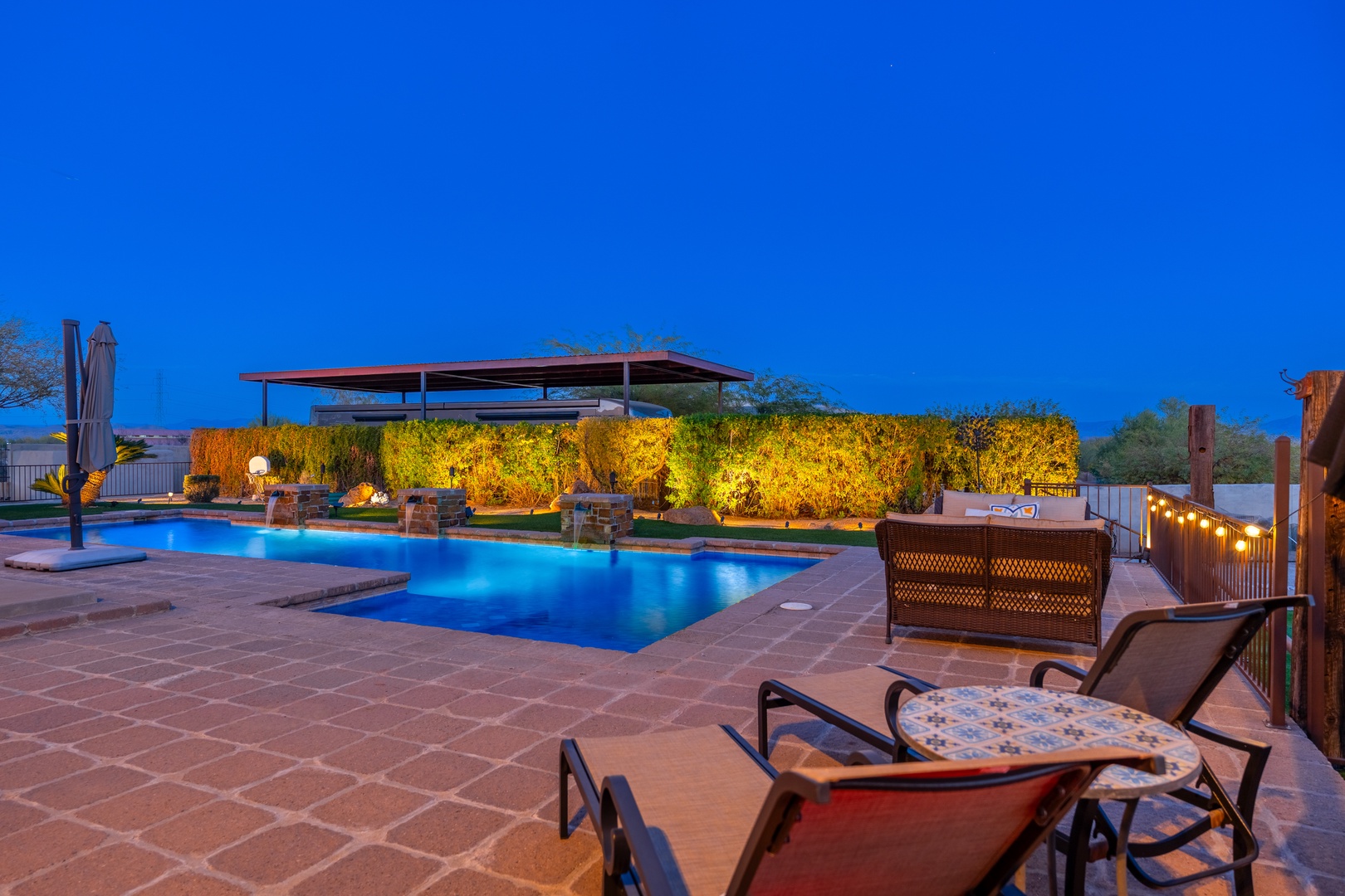 Stunning pool area framed by lush landscaping and warm ambient lighting, perfect for your evening relaxation under the open desert sky.