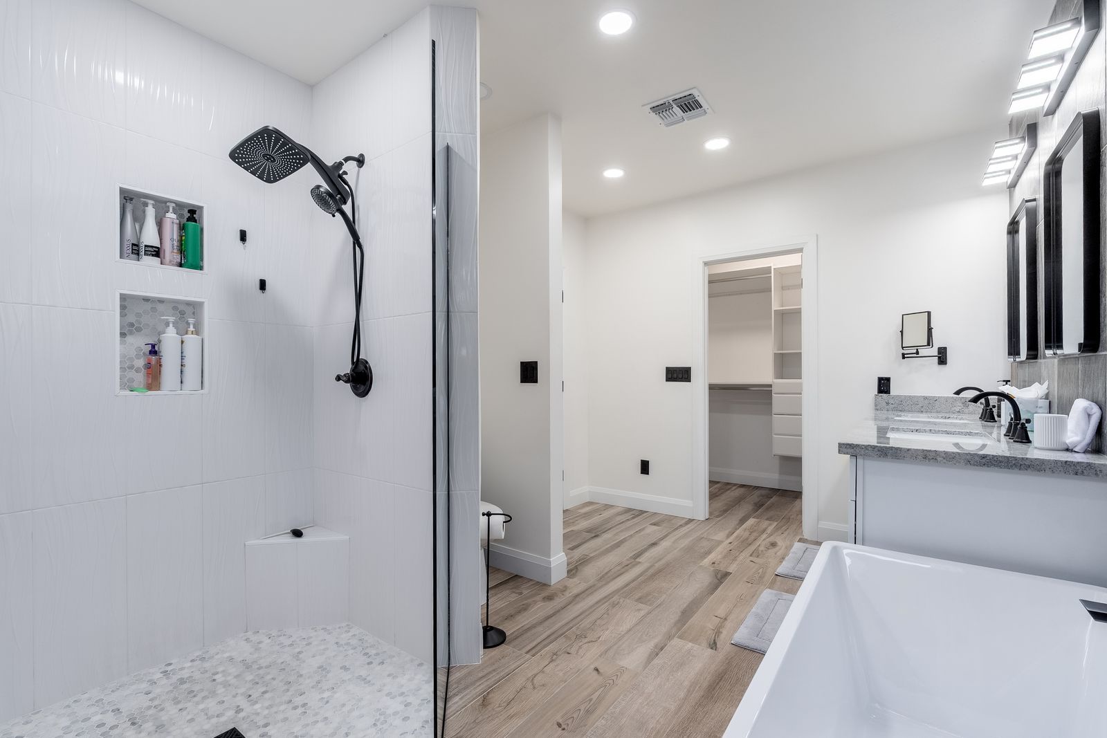 Your spacious bathroom features a sleek walk-in shower, a luxurious soaking tub, and warm wood-look floors that invite you to unwind in comfort and style.