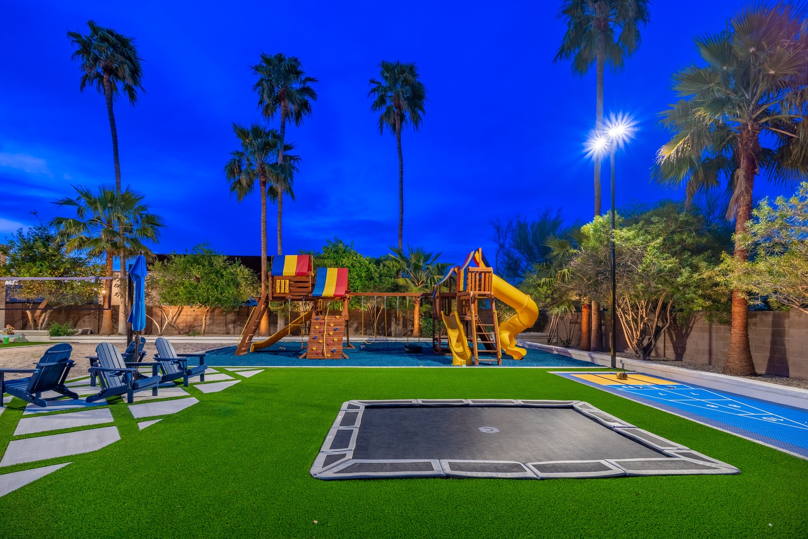 Backyard paradise featuring a sprawling play area with slides, swings, in-ground trampoline, and pool—surrounded by palm trees and illuminated for evening adventures your family will love.