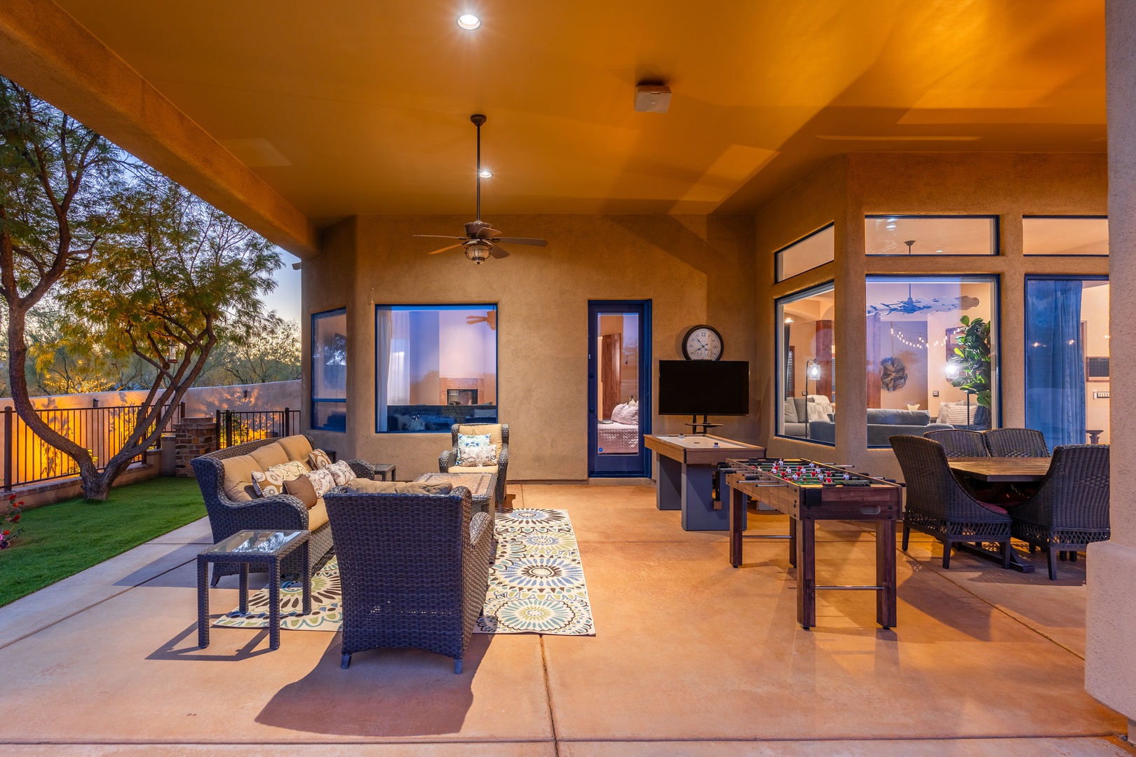 Unwind in your expansive covered patio with comfortable seating, foosball entertainment, and seamless indoor-outdoor living as the desert sky glows at dusk.