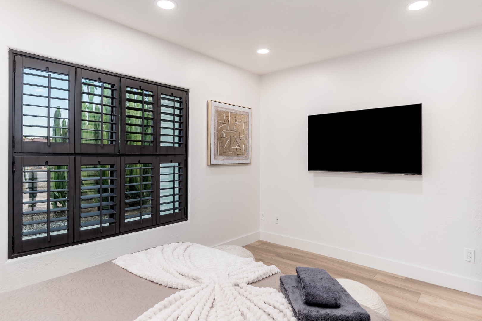 Unwind in your tranquil bedroom featuring a cozy bed, sleek wall-mounted TV, and elegant shutters that frame natural light. Soft linens invite restful nights.