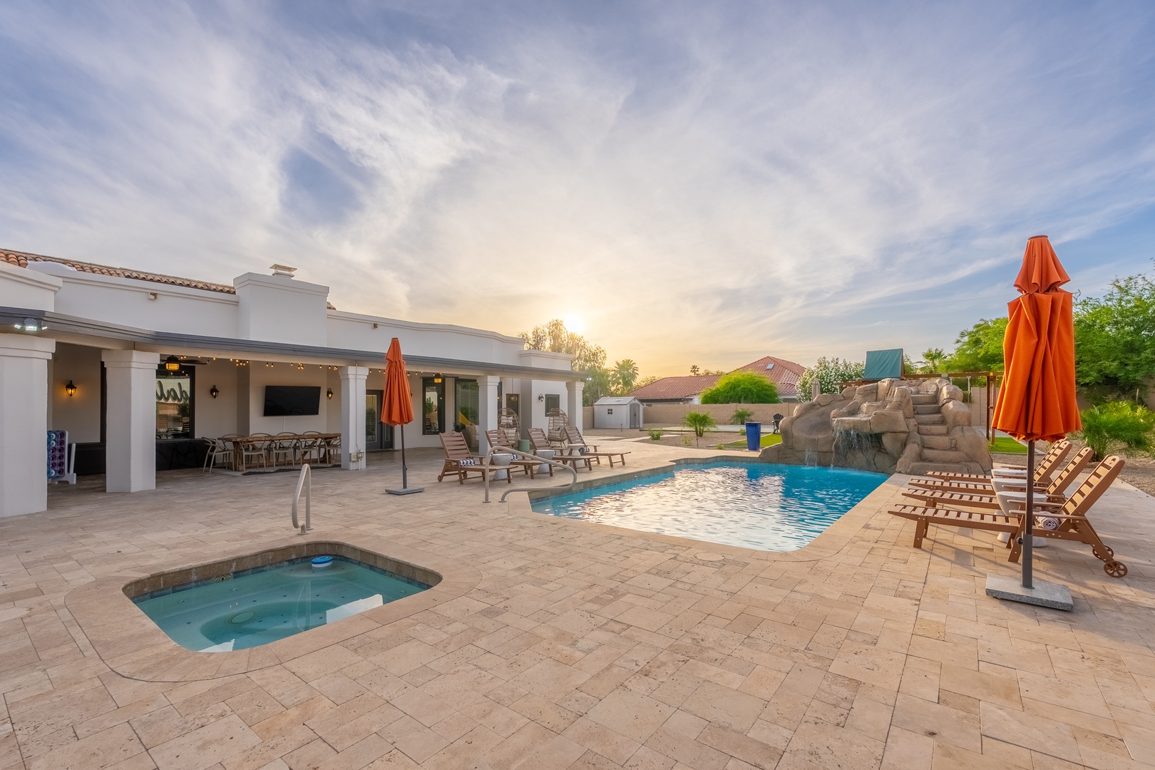 Expansive outdoor oasis with a sparkling pool and hot tub, framed by loungers beneath vibrant umbrellas. Perfect for soaking up warm desert evenings and sunset views.