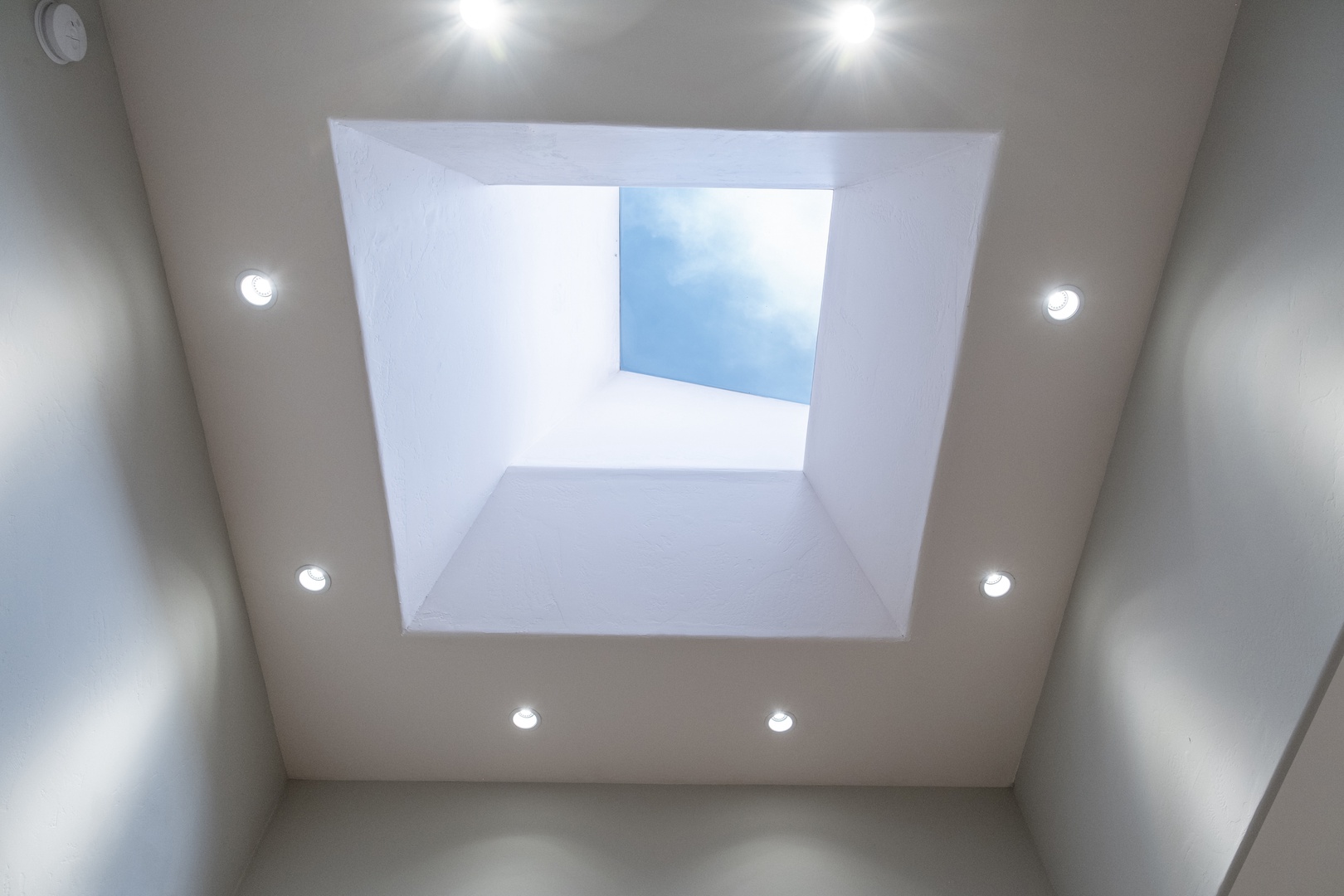 Modern architectural design features a dramatic skylight framing blue sky above, bringing natural light into the interior space and creating an airy, open atmosphere.