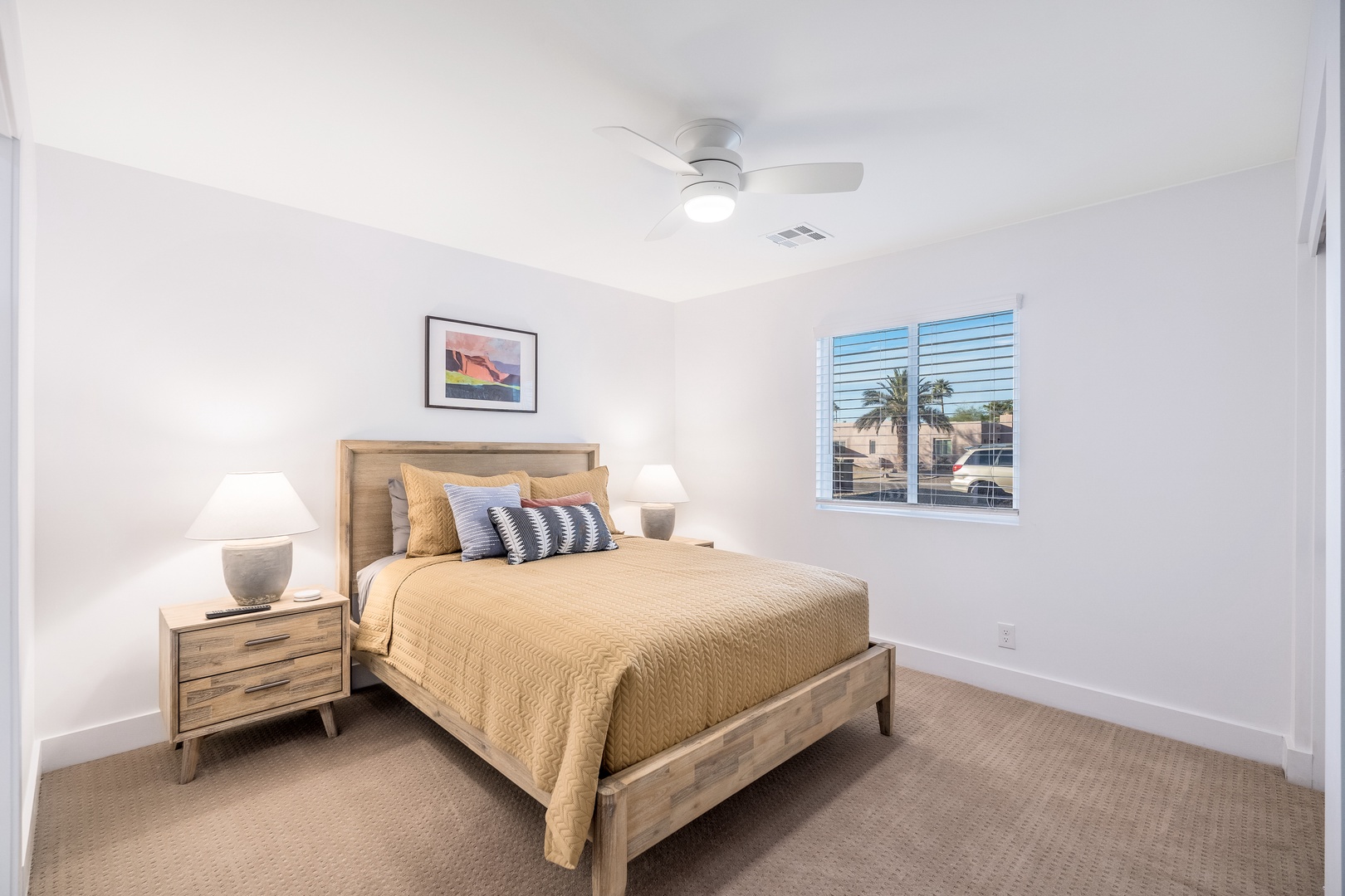 Unwind in your peaceful bedroom featuring a plush queen bed, calming coastal decor, and a ceiling fan to keep you cool. Natural light filters through window blinds as you settle in for a restful stay.
